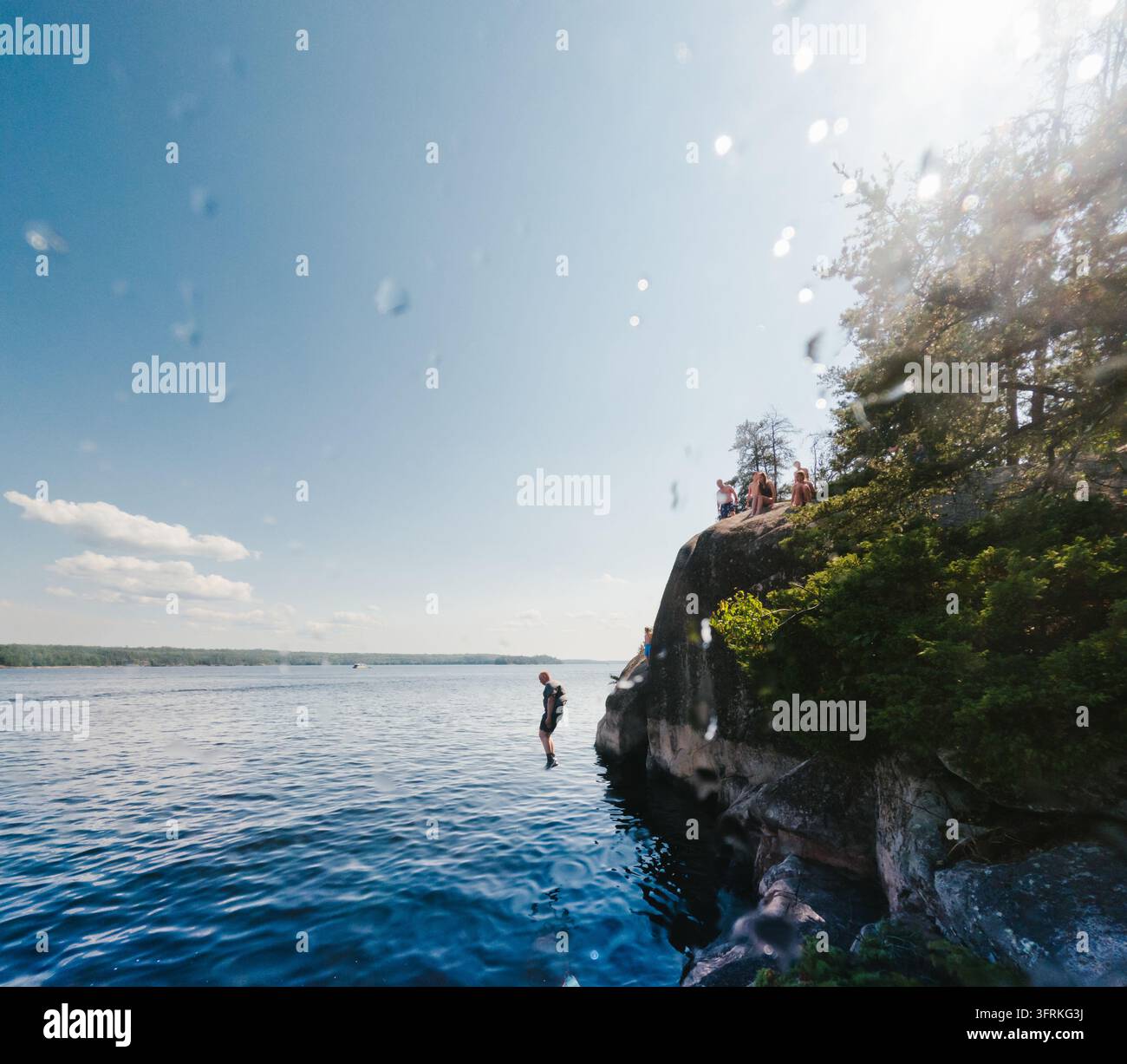 Uomo che salta da una scogliera in un lago in una giornata di sole estiva Foto Stock