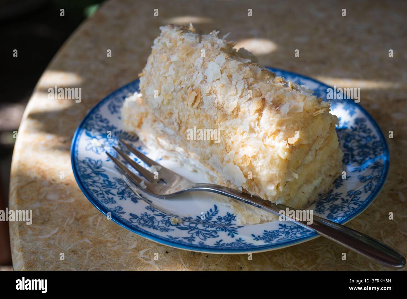Una fetta di torta Napoleone friabile è servita su un piatto a motivi blu e bianchi con una forchetta Foto Stock