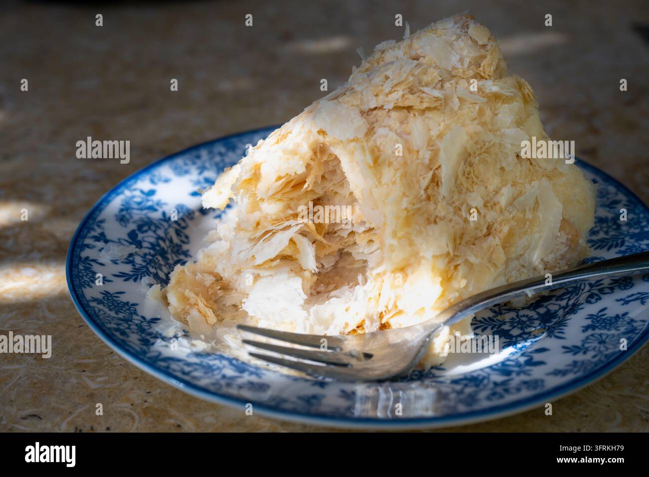 Una fetta di torta Napoleone friabile è servita su un piatto a motivi blu e bianchi con una forchetta. Foto Stock