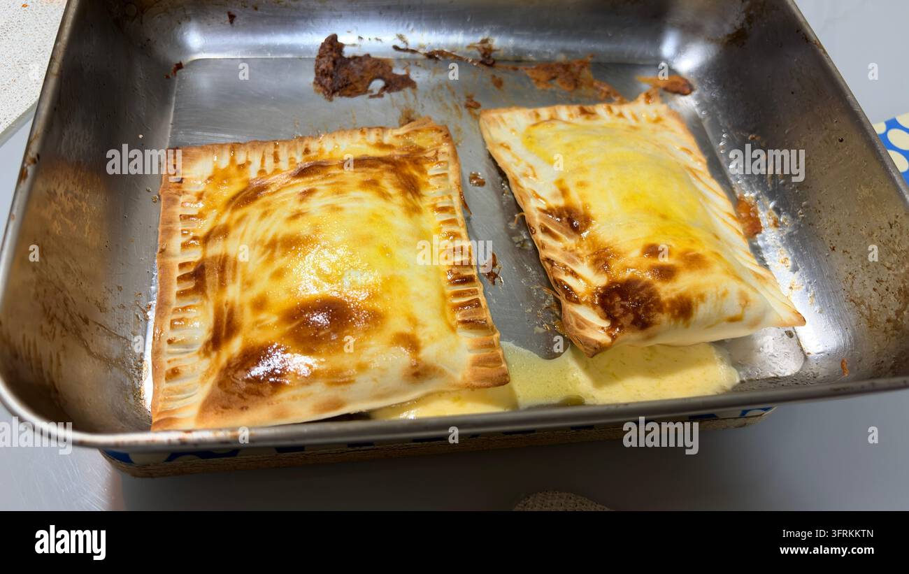 Frittelle di pasta dorate al forno con ripieno fuso che riposano in una teglia di metallo Foto Stock