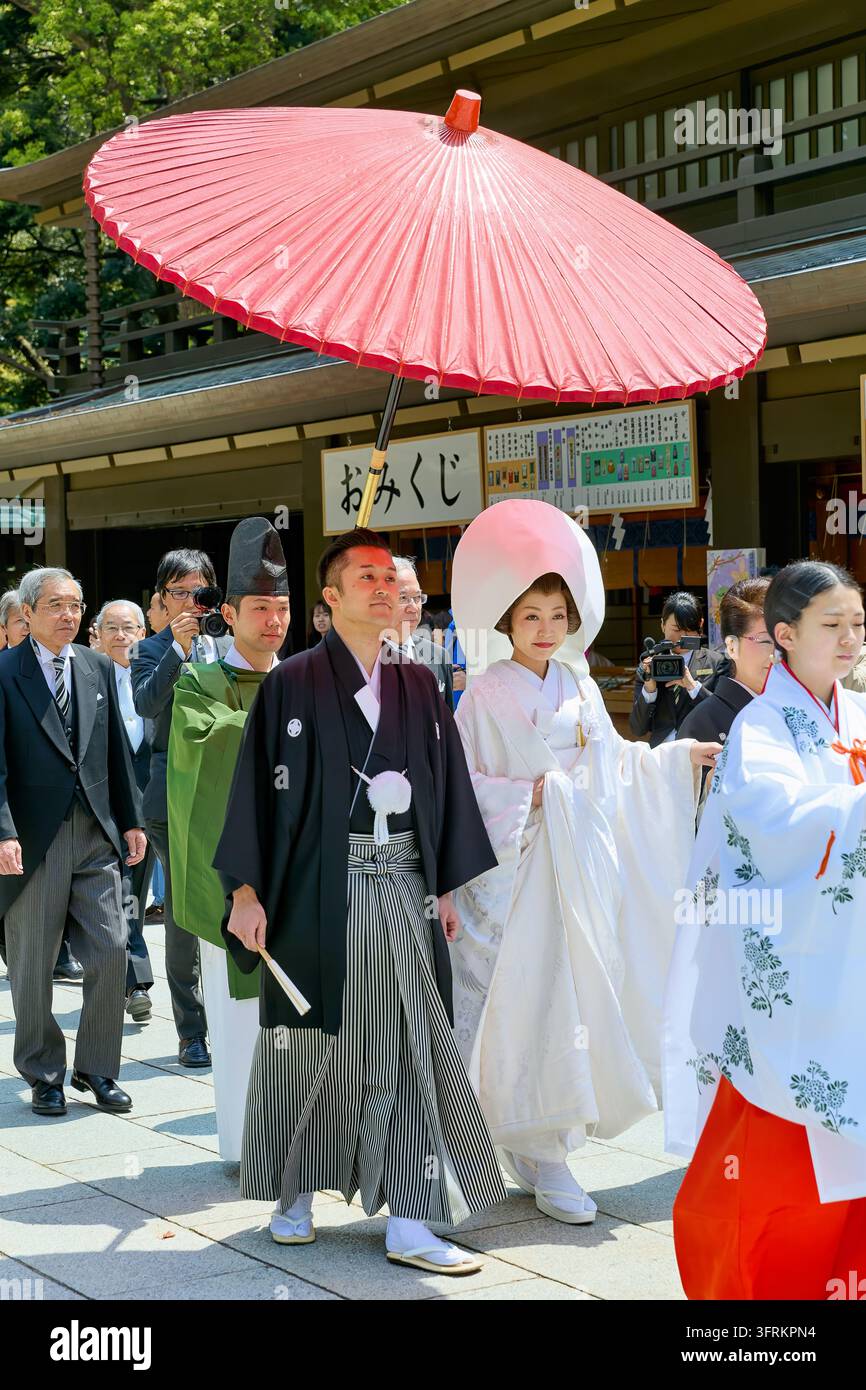 Sposa in kimono shiromuku bianco e sposo in hakama seguono una sacerdotessa, con un sacerdote e gli ospiti dietro, durante una cerimonia nuziale giapponese Foto Stock