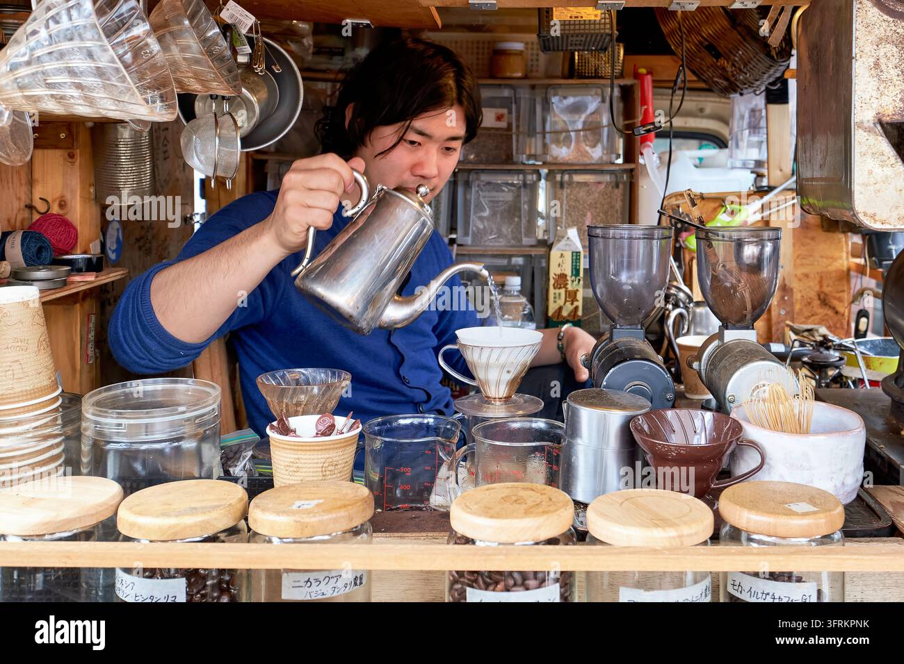 Il venditore prepara il caffè a goccia a mano con un bollitore a collo d'oca e un filtro conico in ceramica in un chiosco del caffè all'aperto a Tokyo, Giappone, con barattoli di chicchi Foto Stock