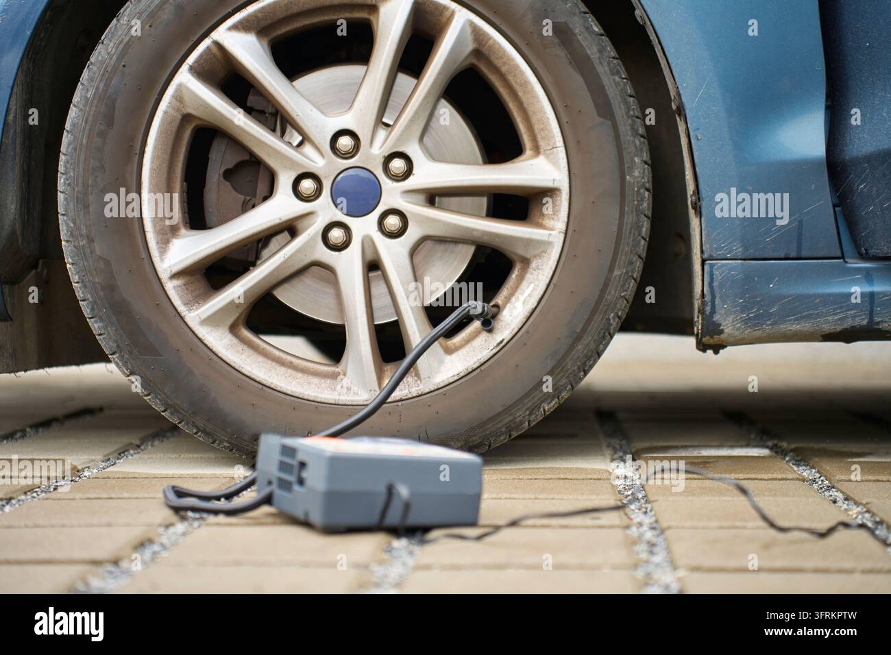 Pompa ad aria portatile collegata alla valvola di uno pneumatico dell'auto accanto alla ruota. Concetto di gonfiaggio e controllo della pressione dei pneumatici Foto Stock