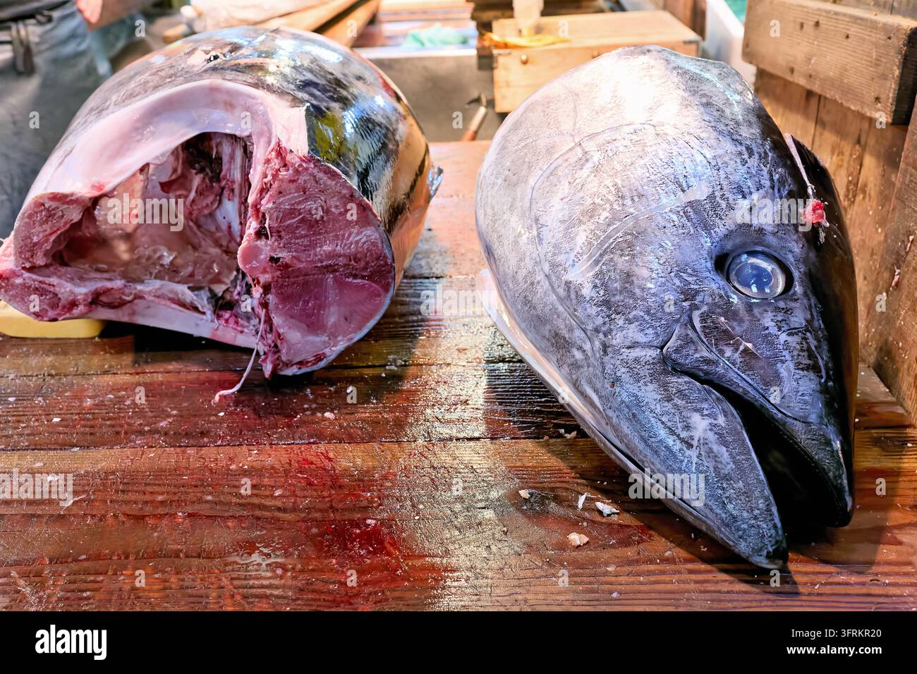 Testa mozzata di un tonno grande accanto a una sezione anteriore macellata su un tagliere di legno bagnato in un mercato ittico di Tokyo Foto Stock