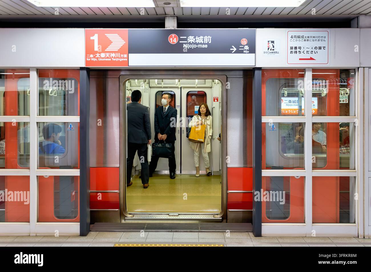 I pendolari si trovano in un vagone dietro le porte aperte dei parabordi della metropolitana comunale di Kyoto in Giappone, un uomo indossa una mascherina. Foto Stock