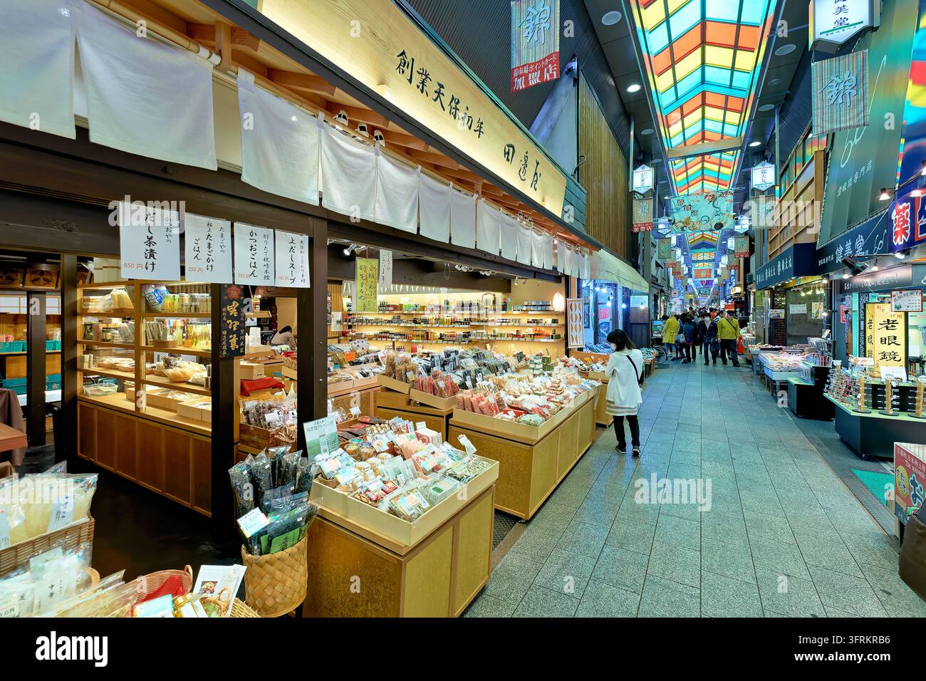 I clienti percorrono una strada coperta fiancheggiata da bancarelle che vendono fiocchi di bonito, alghe e prodotti Dashi sotto un tetto di vetro colorato a Kyoto. Foto Stock