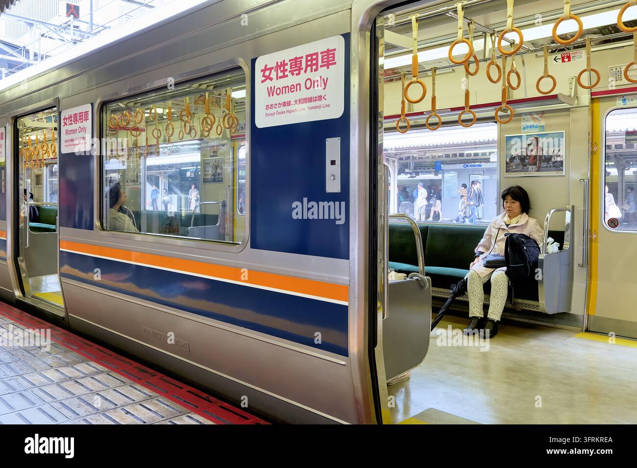 Segnale giapponese e inglese che indica un vagone riservato alle donne su un treno pendolare della serie 207 mentre una passeggera è seduta su una panchina all'interno Foto Stock
