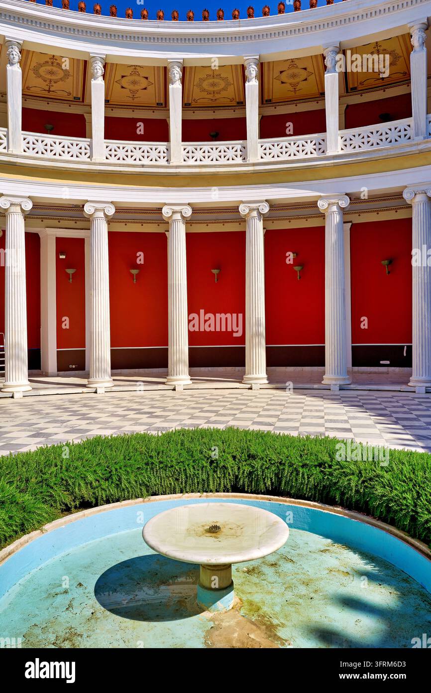 Colonne di marmo ioniche, mura rosse e una fontana nel peristilio neoclassico del Zappeion del XIX secolo ad Atene in una mattinata estiva soleggiata Foto Stock