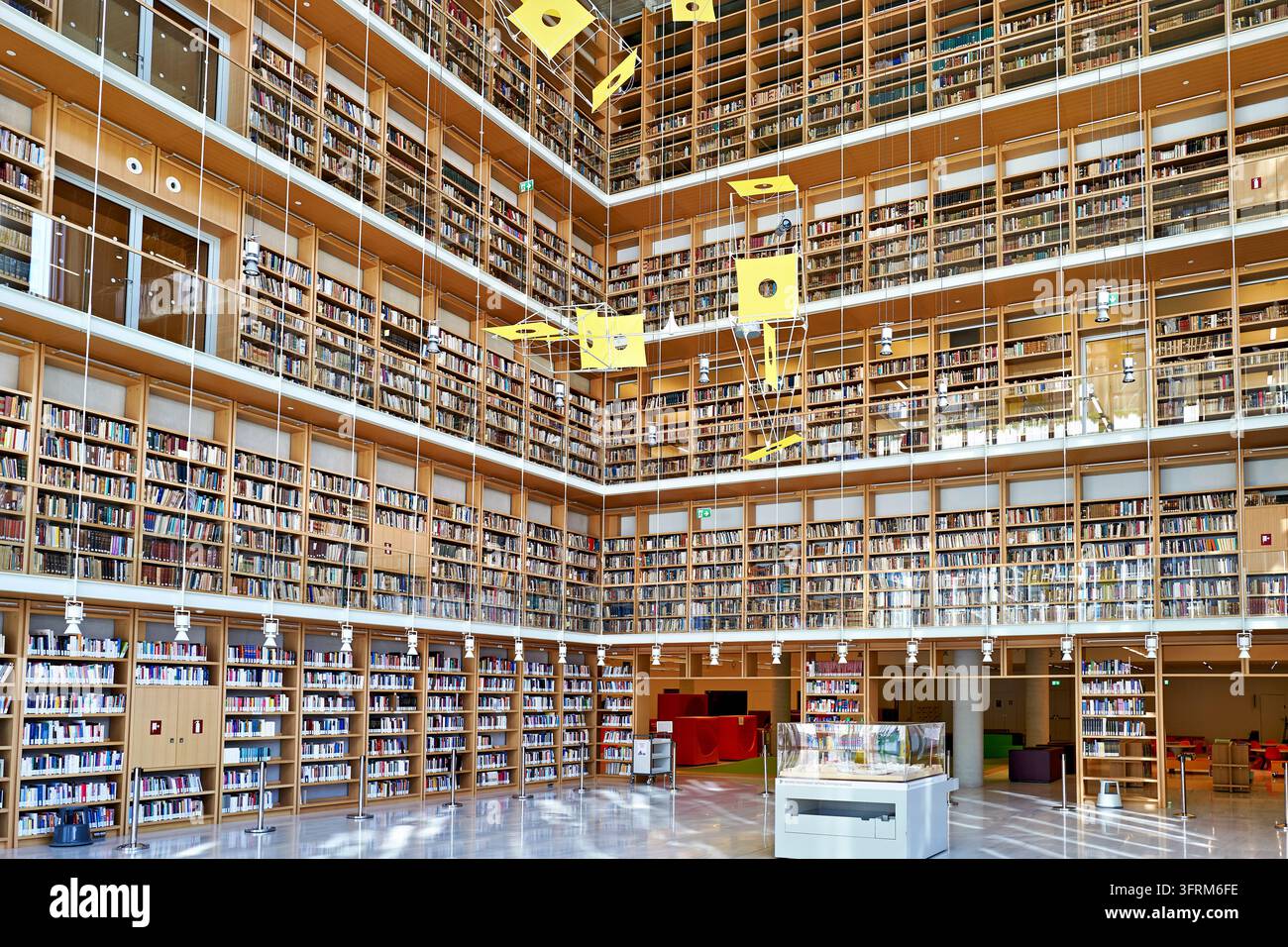 Scaffali librari in legno multipiano si innalzano attorno a un luminoso atrio con un'opera d'arte sospesa gialla al Centro Culturale della Fondazione Stavros Niarchos Foto Stock