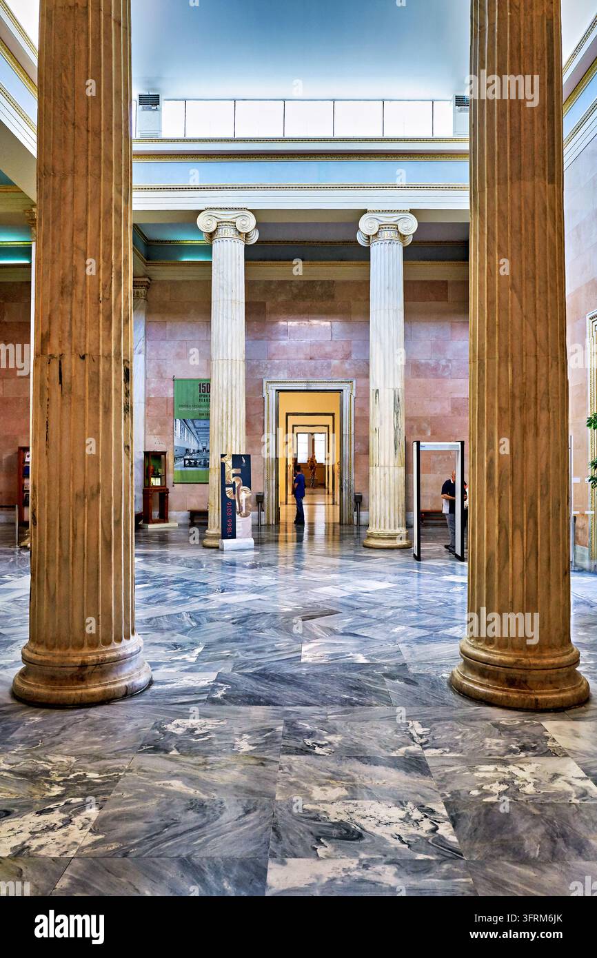 Piloni scanalati, pavimento in marmo con venature grigie e pareti in marmo rosa nella lobby del museo nazionale greco, con un cancello di sicurezza e una fila di gallerie Foto Stock
