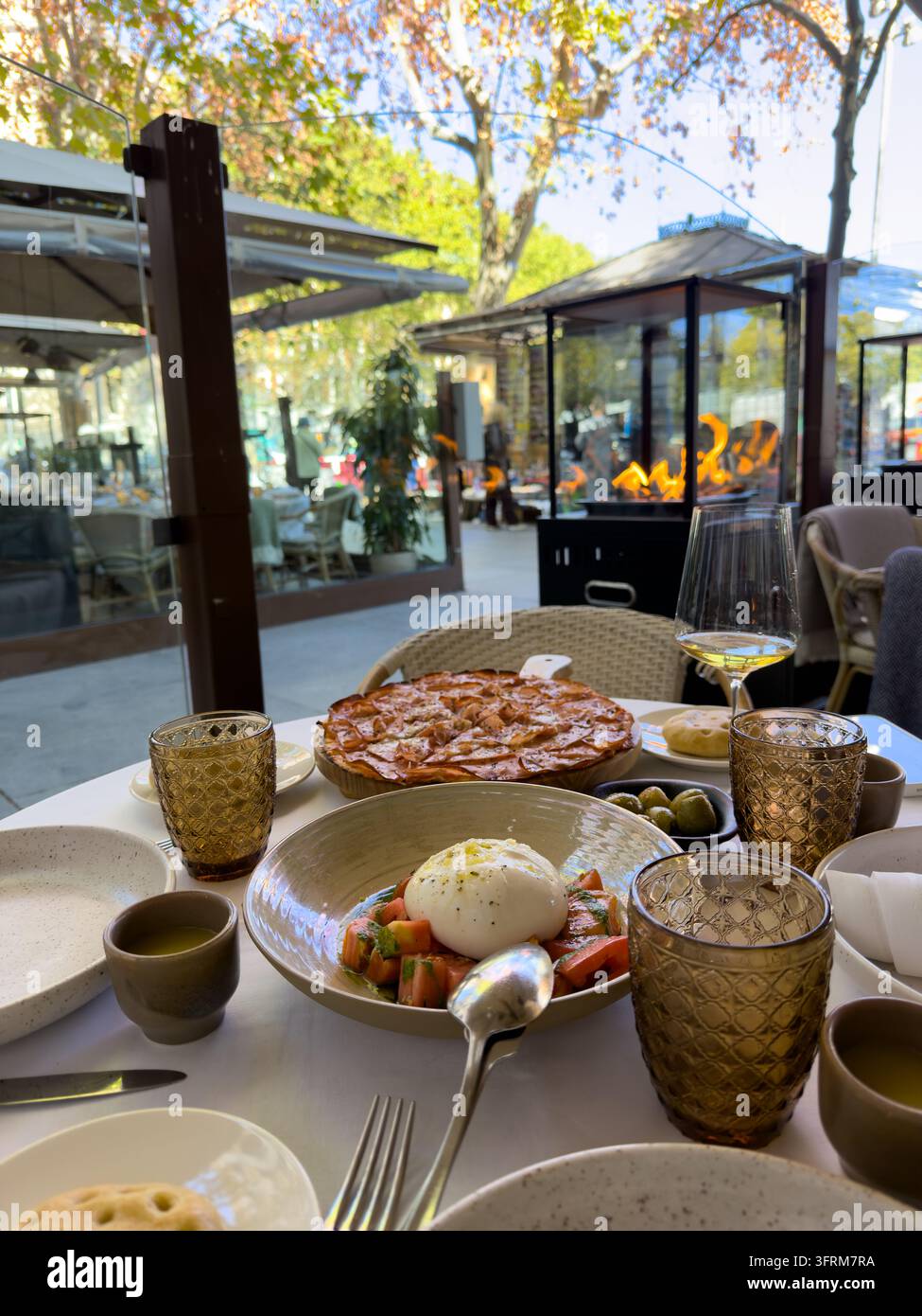 MADRID, SPAGNA - 09 OTTOBRE 2026 Insalata di burrata e pane azzimo riposano su un tavolo da ristorante all'aperto accanto a vino e olive. Ambientazione di pasto mediterraneo featu Foto Stock
