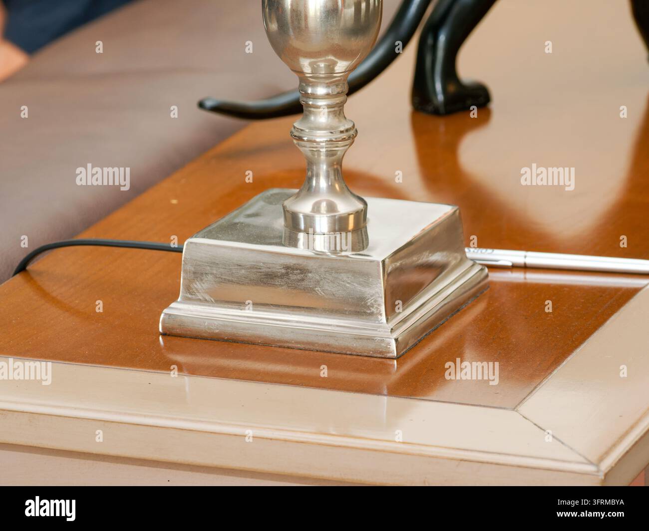Primo piano di una base di lampada argentata su un tavolo di legno all'interno. Foto Stock