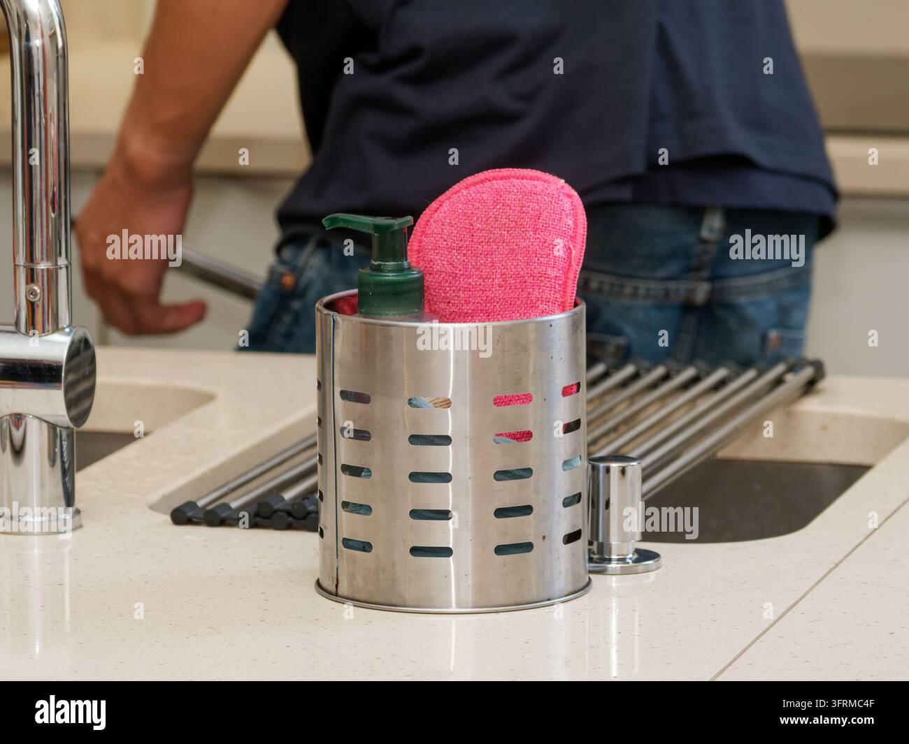 Piano di lavoro della cucina con un portautensili in acciaio contenente una spugna per lavare i piatti e un dispenser di sapone liquido. Foto Stock