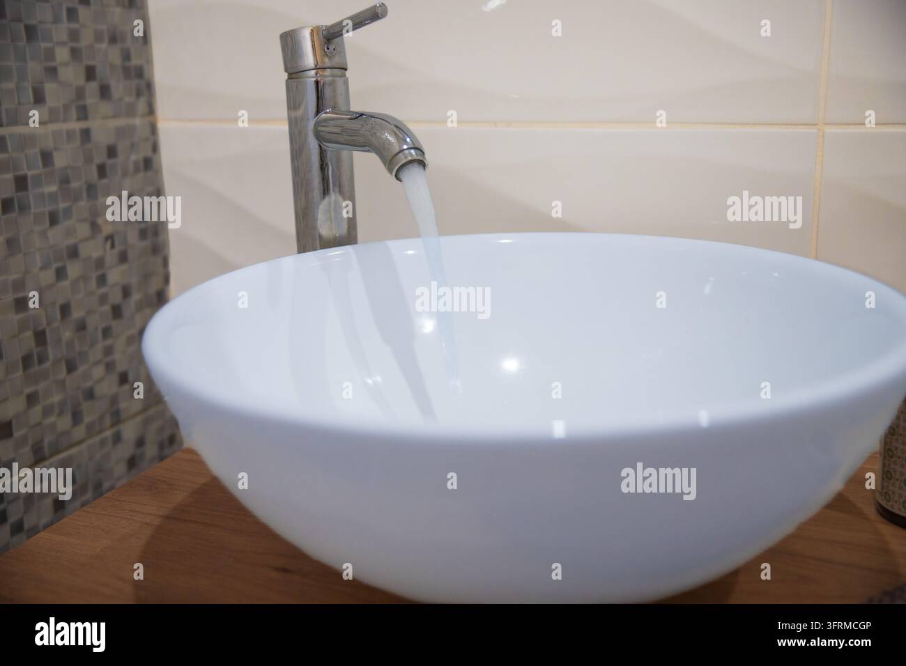 Acqua corrente da un rubinetto cromato in un lavandino bianco da bagno Foto Stock