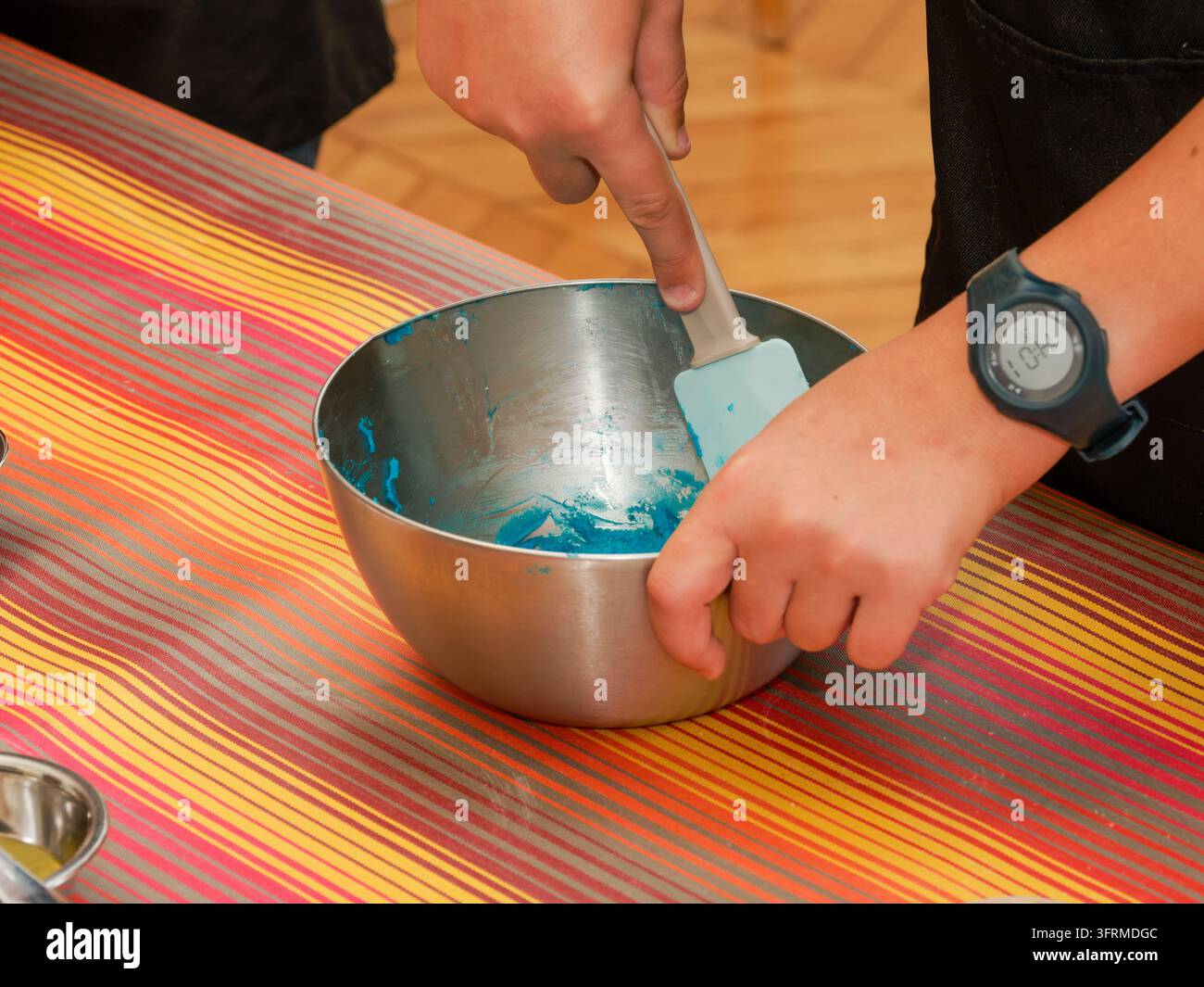 Mani che mescolano una sostanza blu in una ciotola di acciaio inossidabile su una tovaglia a righe. Foto Stock