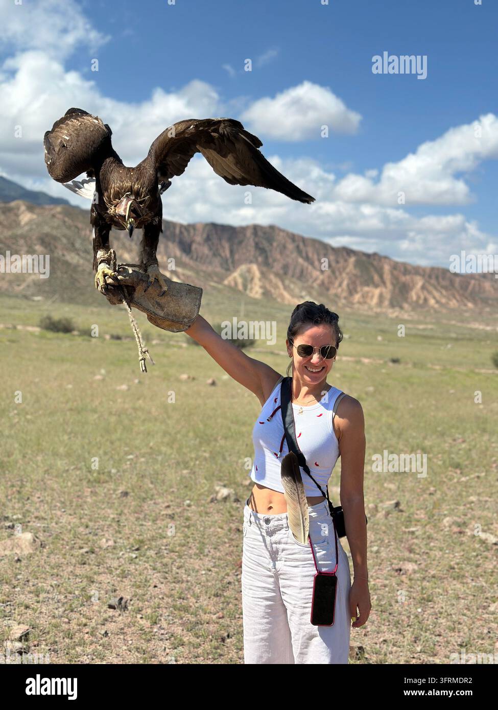 Alate: una viaggiatrice sorridente tiene un aquila reale mentre spande le sue ali vicino al canyon Skazka in Kirghizistan Foto Stock