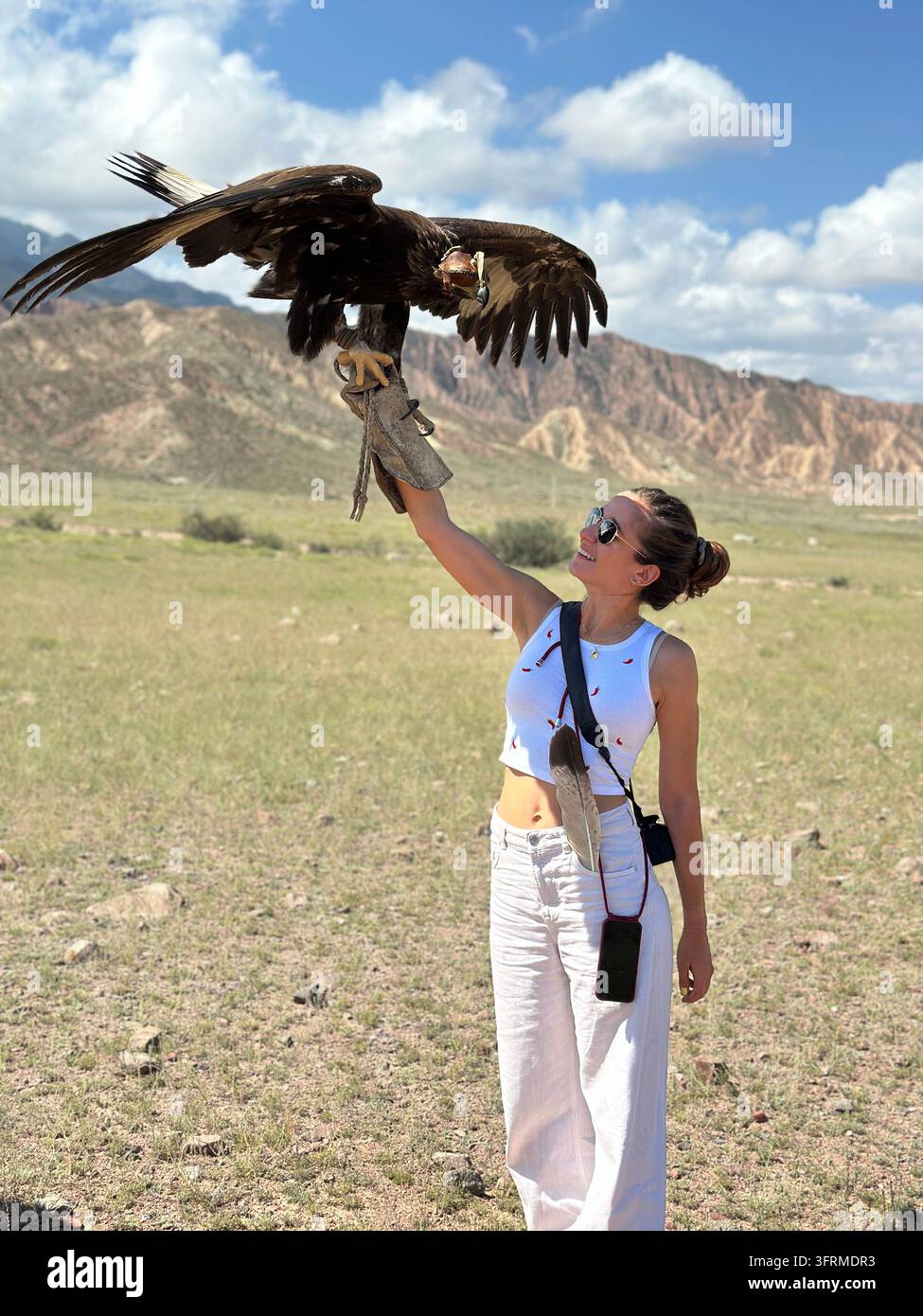 Pronto per il decollo: un aquila reale sbatte le sue enormi ali sul braccio guantato di un viaggiatore vicino al Canyon Skazka in Kirghizistan Foto Stock