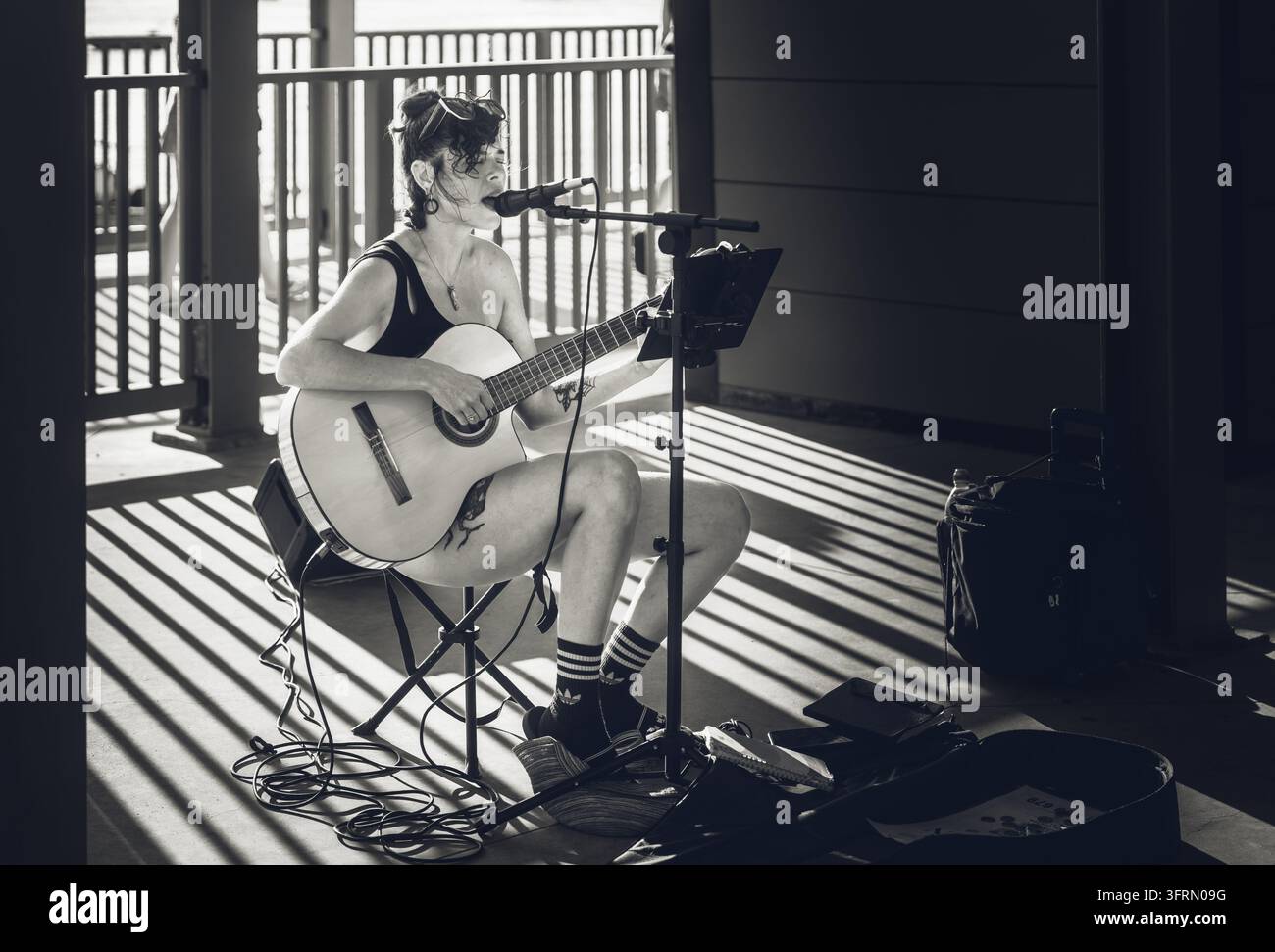 Tavira, Portogallo, 19 agosto 2026. Musicista di strada suona la chitarra tra forti ombre e luce solare. Foto Stock