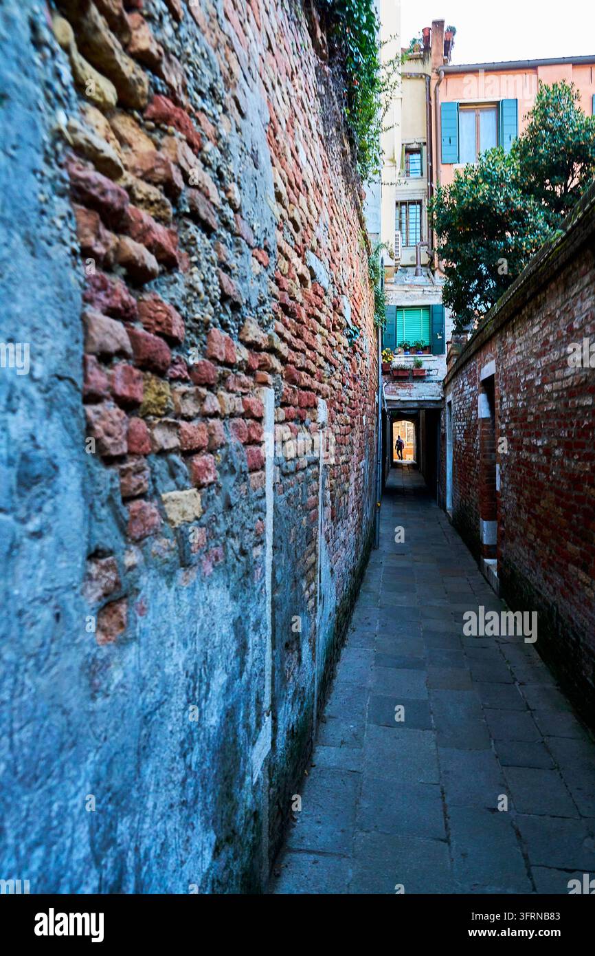 Stretta via storica a Venezia, Italia, con muri di mattoni consumati, pavimentazione in pietra e architettura veneziana tradizionale. Foto Stock