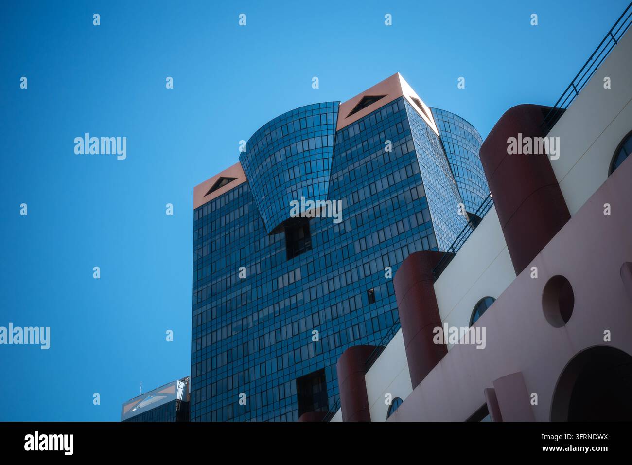 Vista stradale a basso angolo di una moderna torre di uffici in vetro a Lisbona, Portogallo, con facciate curve riflettenti blu accanto a un edificio bianco con cy rosso Foto Stock