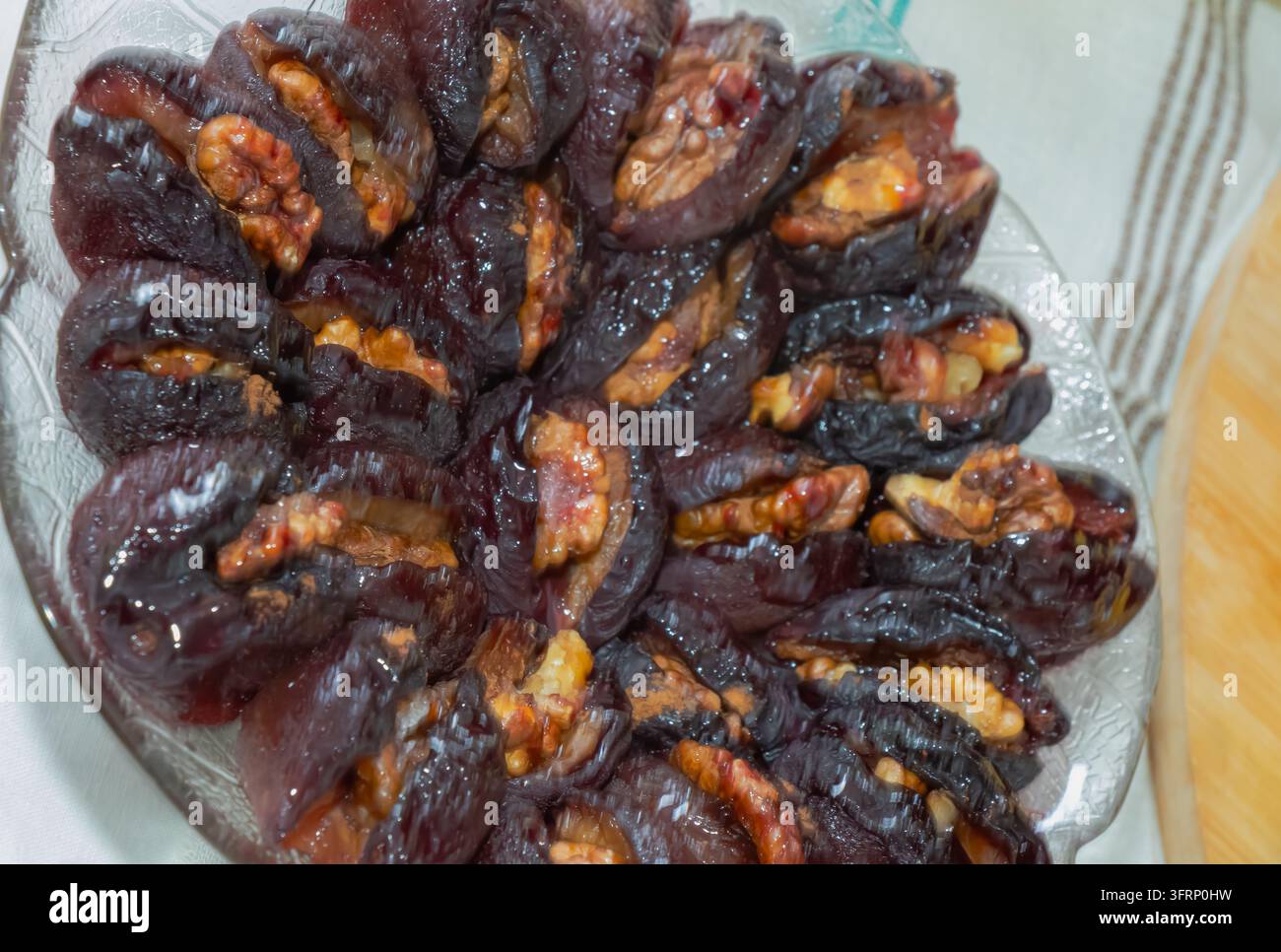 Prima vista di prugne secche scure ripiene di pezzi di noce e servite su un piatto di vetro, creando un ricco dessert tradizionale di frutta secca con natura lucida Foto Stock