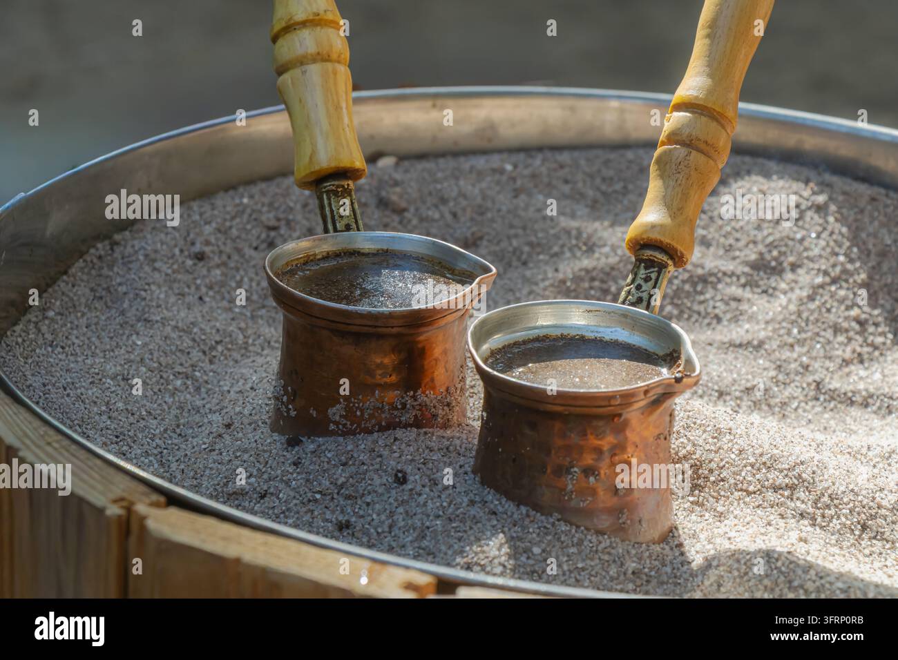 Prima vista di due piccole cezve di rame che preparano il caffè nella sabbia calda, mostrando un metodo di preparazione tradizionale con manici di legno e metallo rustico caldo Foto Stock