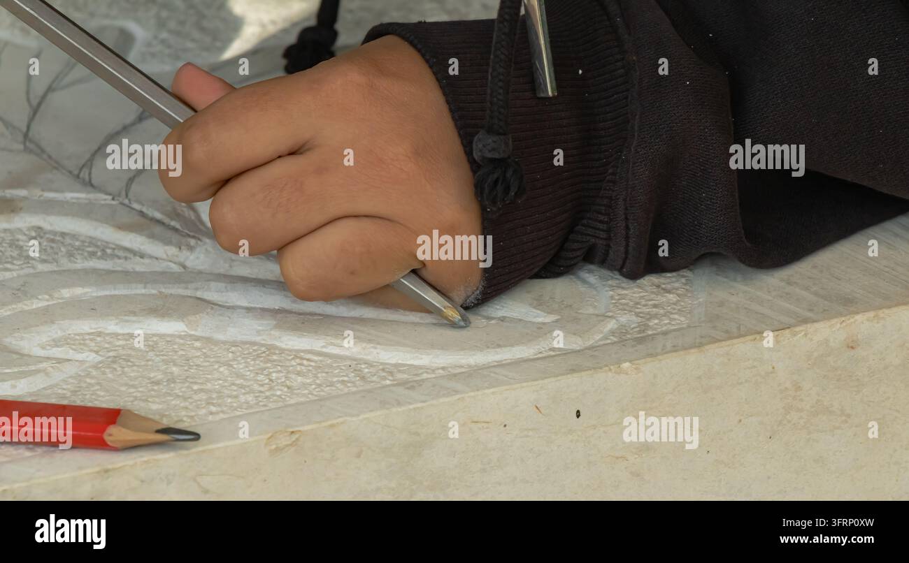 Primo piano di una mano che intaglia un motivo decorativo su una superficie di pietra chiara con uno strumento metallico, mostrando artigianalità, dettagli in rilievo e artigiano Foto Stock