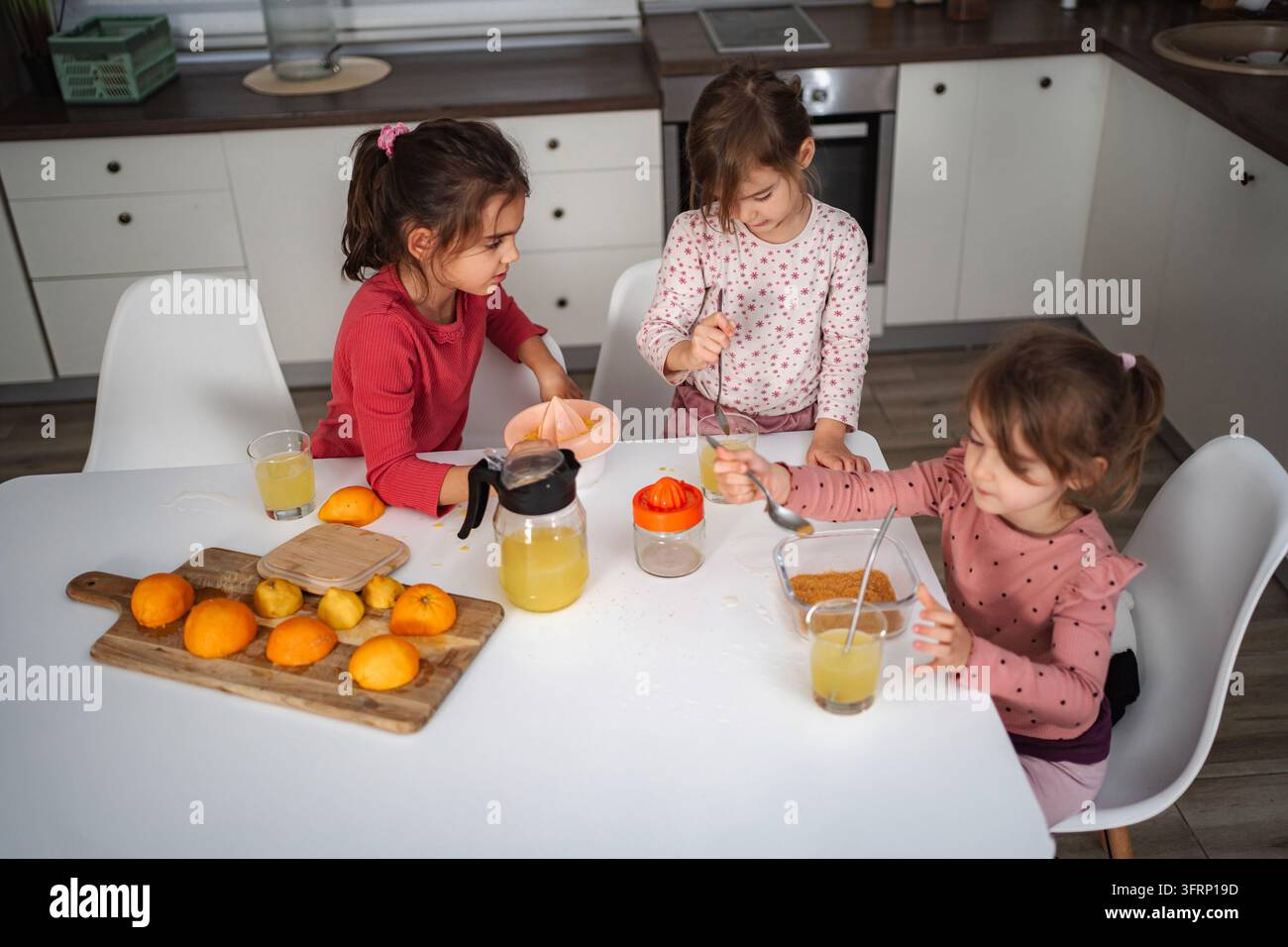 Ragazze che preparano succo d'arancia fresco in cucina, imparano a preparare una bevanda sana Foto Stock