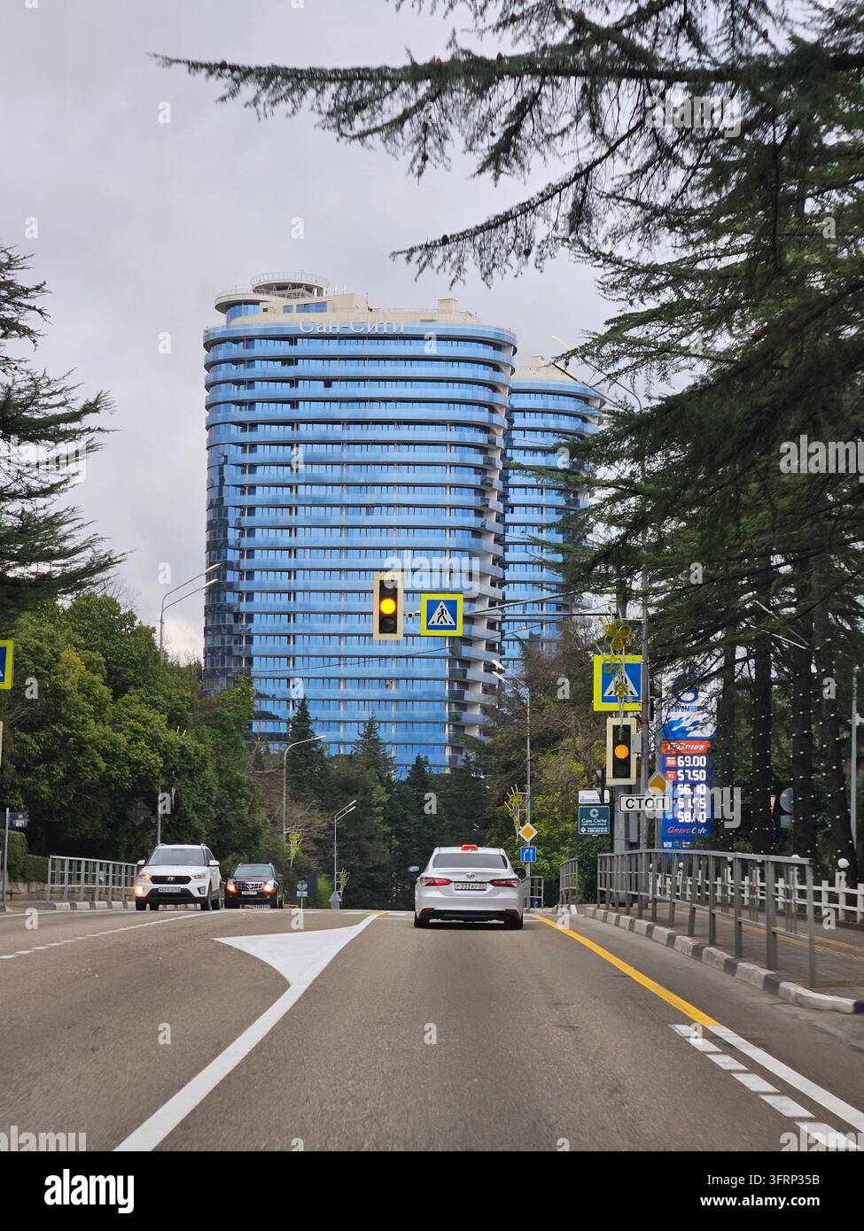 SOCHI - 31 DIC. 2023: Un'auto percorre una strada con semaforo vicino ad un edificio alto. Il semaforo è giallo, indicando che il conducente deve rallentare ed essere pronto a fermarsi se necessario Foto Stock