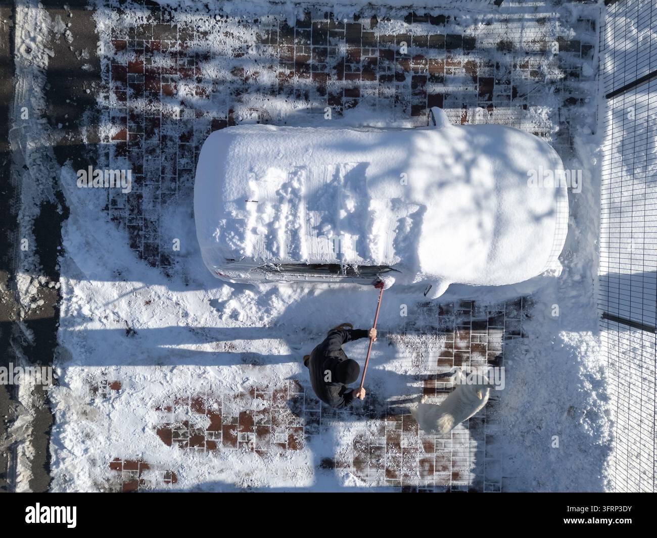 Una persona pulisce un'auto coperta di neve durante una fredda mattina d'inverno in una zona residenziale. Foto Stock