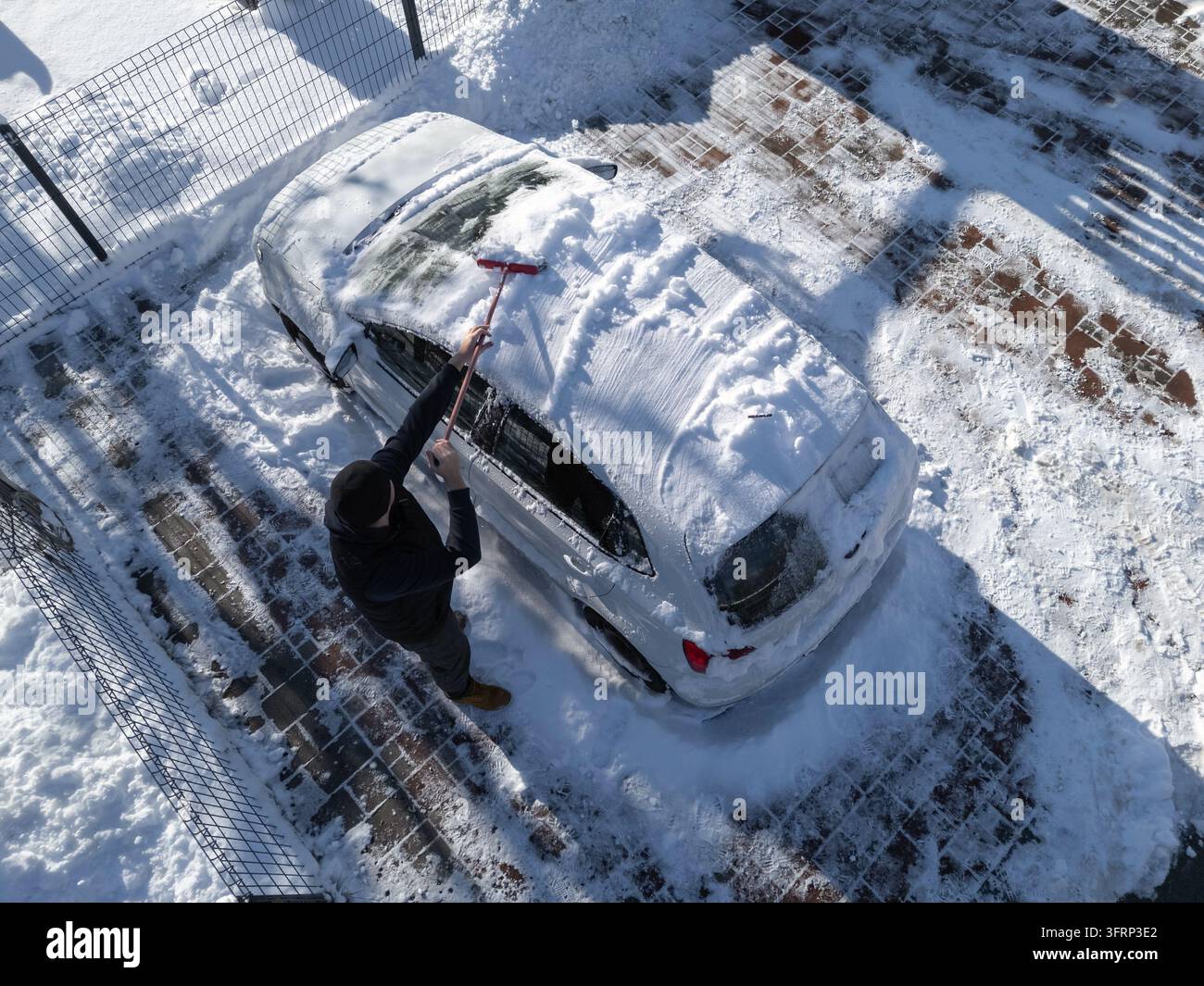 Un uomo spazza la neve da un'auto al mattino presto. Fa freddo e il terreno è coperto di neve. Foto Stock