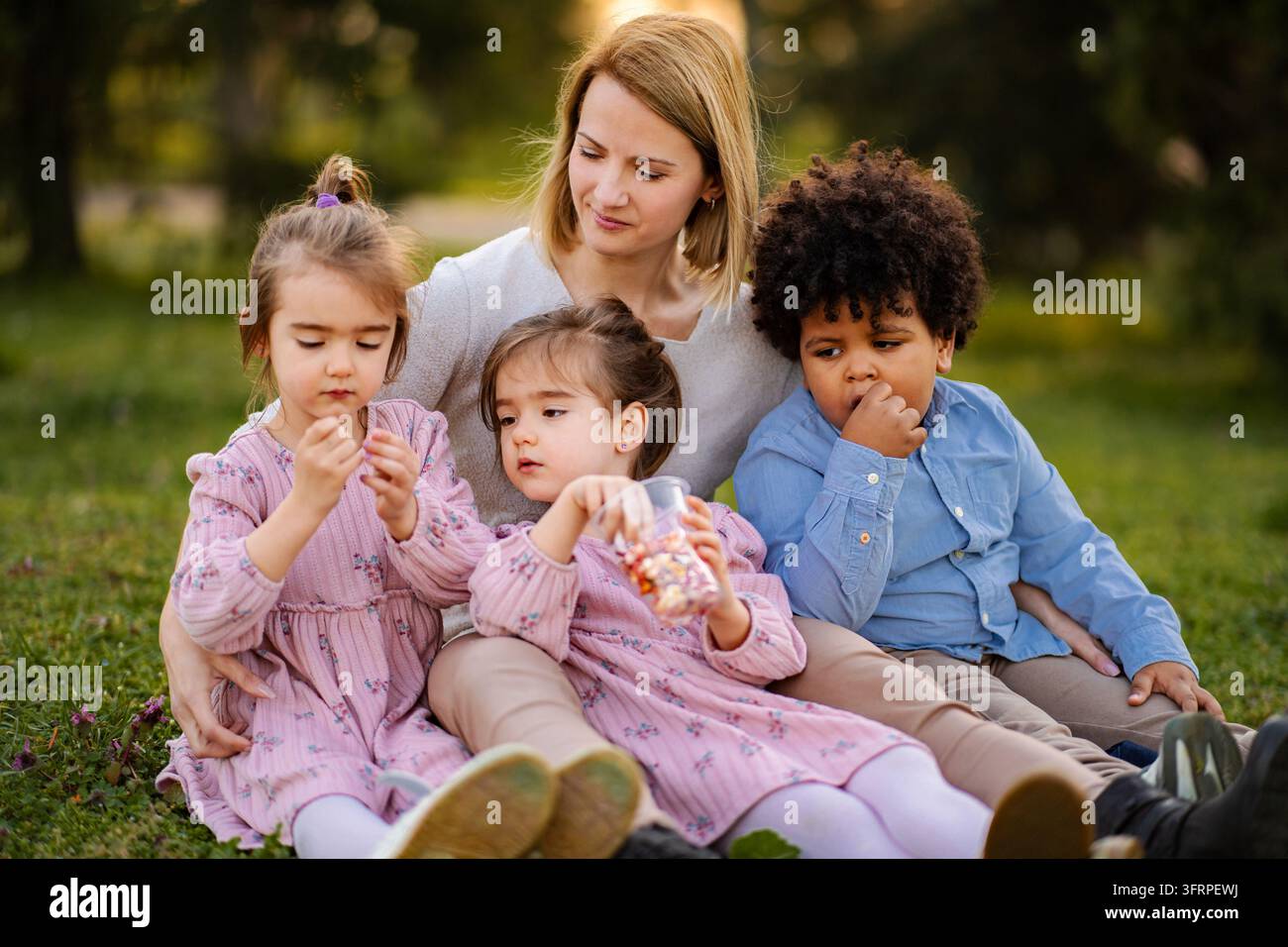 Madre seduta con tre bambini che mangiano caramelle nel parco Foto Stock