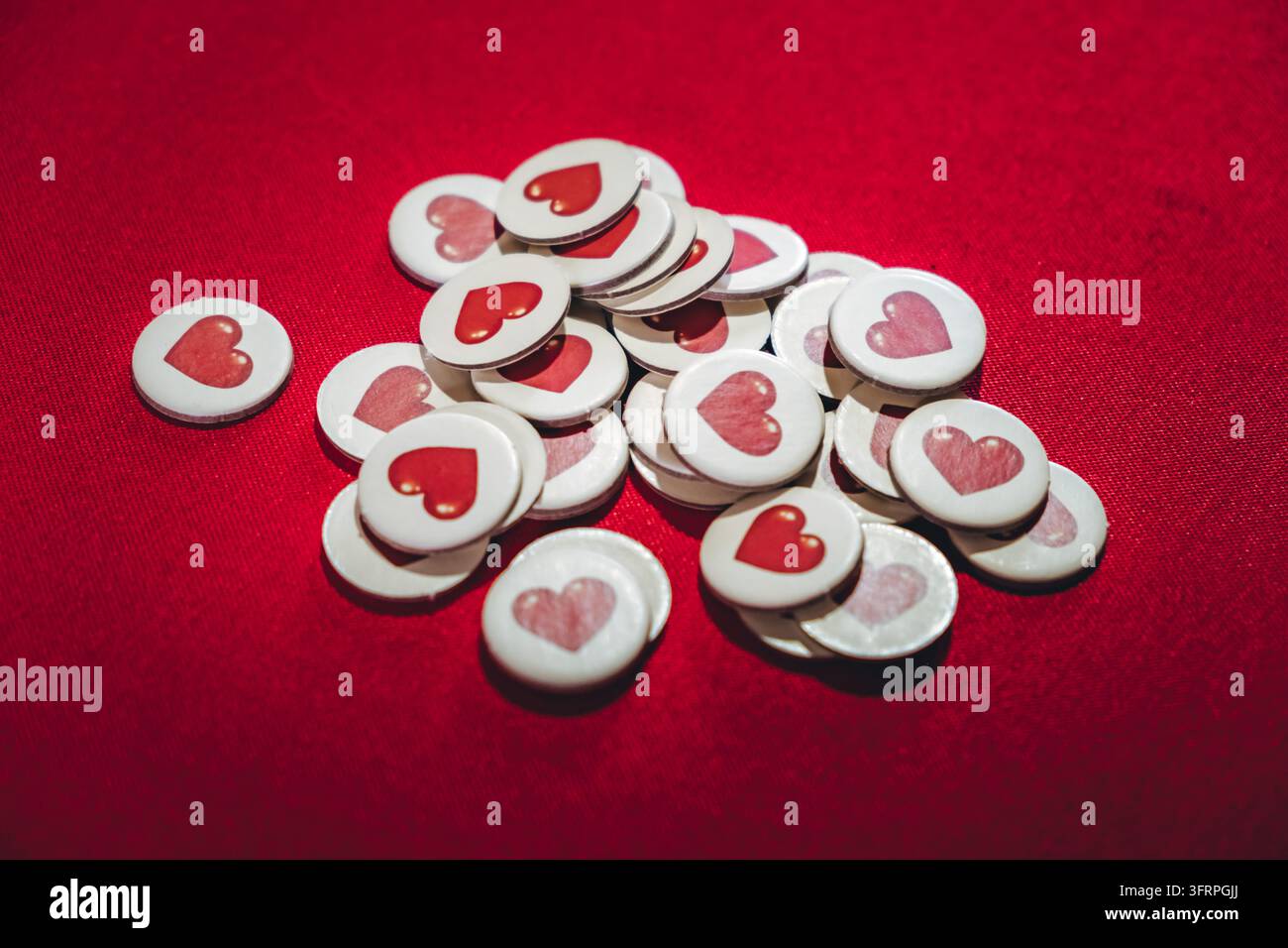 Gettoni da gioco con cuori su sfondo rosso tavolo. Forma rotonda. Molti pezzi. Salute e vita nel gioco. Simbolo d'amore. Gioco da tavolo per bambini. In Foto Stock