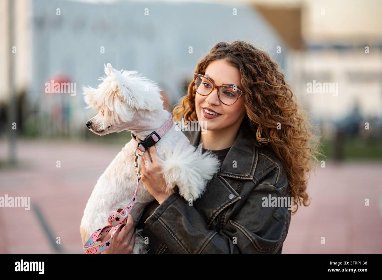 Giovane donna adulta che tiene al guinzaglio un simpatico cane bianco Foto Stock