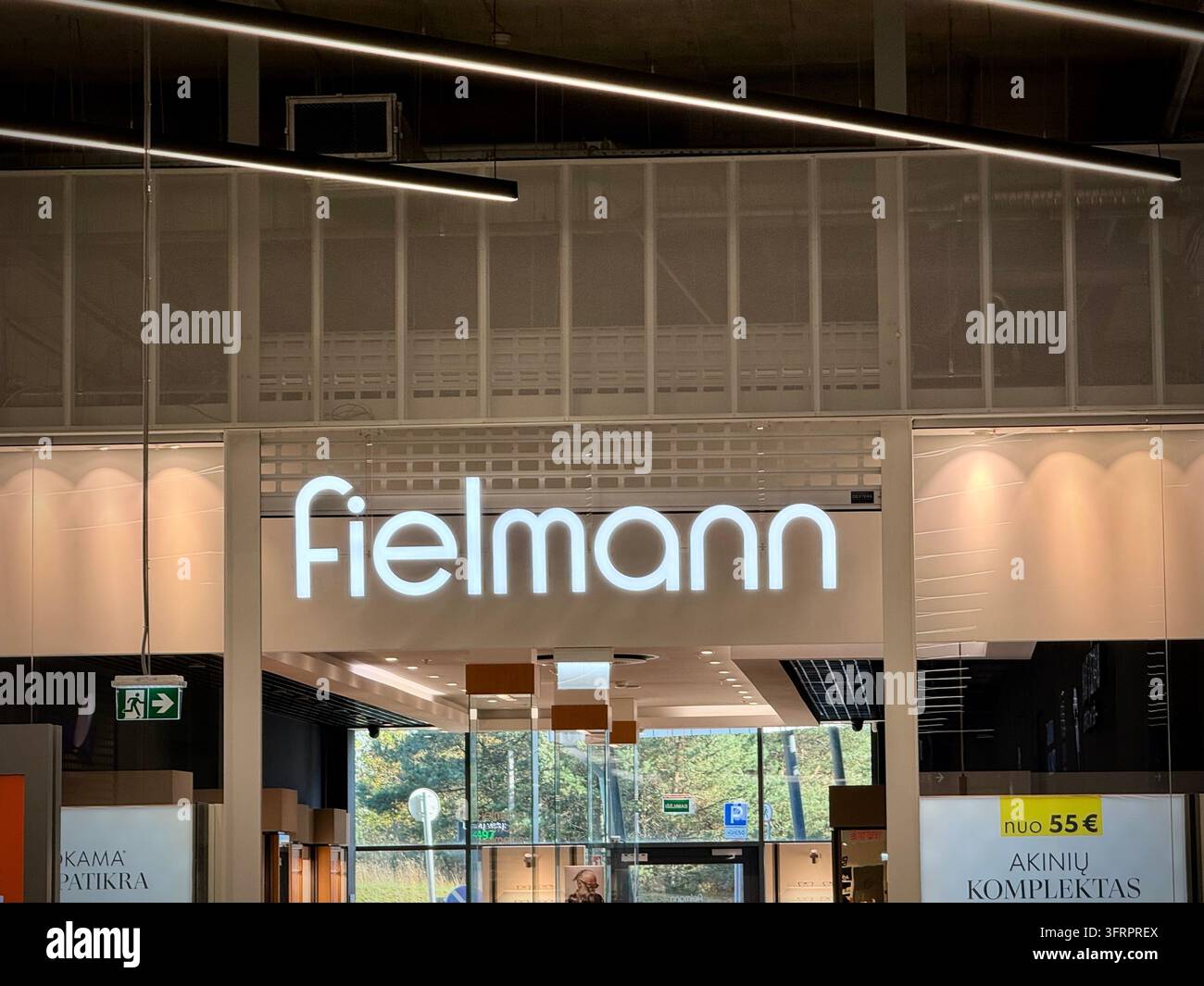 Una fotografia orizzontale che cattura il cartello illuminato bianco del negozio ottico Fielmann all'interno di un centro commerciale moderno, mostrando l'illuminazione dell'ingresso del negozio, i - Immagine stock catturata con smartphone