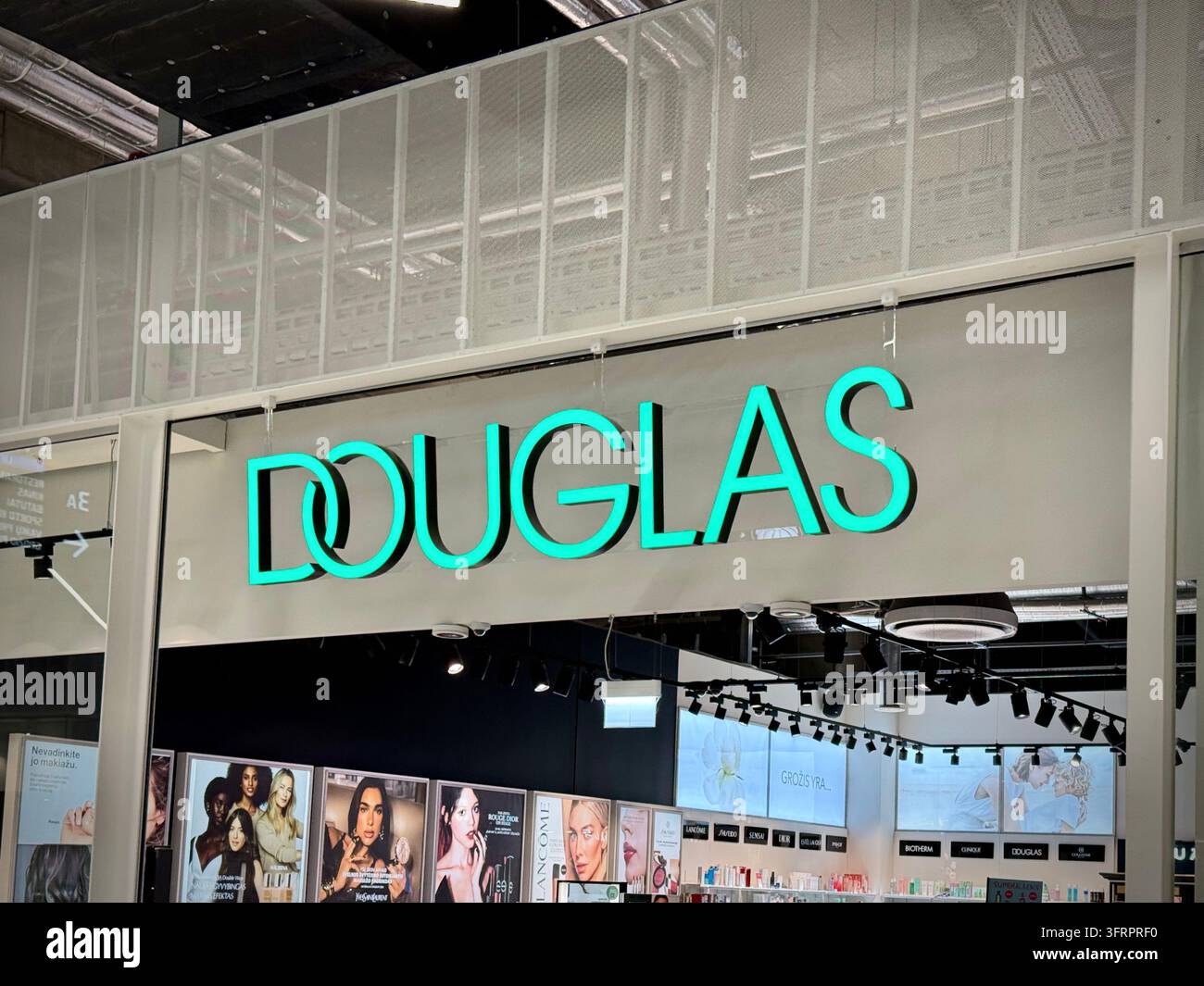 Una fotografia orizzontale che cattura l'insegna illuminata turchese di Douglas montata sopra l'ingresso di un negozio di cosmetici e profumeria all'interno - Immagine stock catturata con smartphone