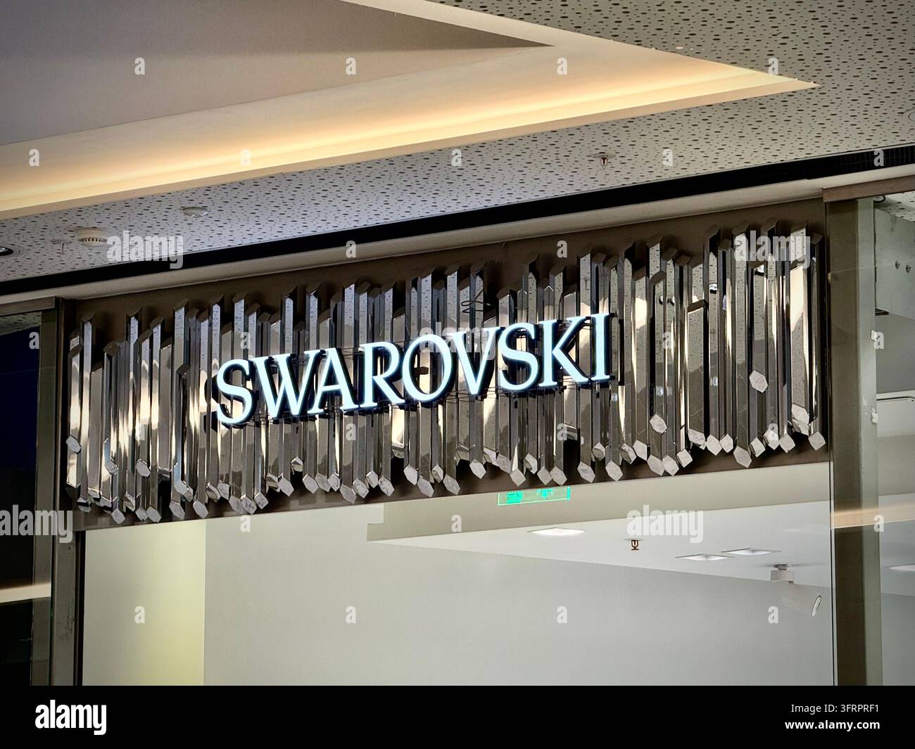 Una fotografia orizzontale in primo piano che cattura il logo illuminato del marchio Swarovski montato su uno sfondo decorativo di aste di cristallo metallico sfaccettate - Immagine stock catturata con smartphone