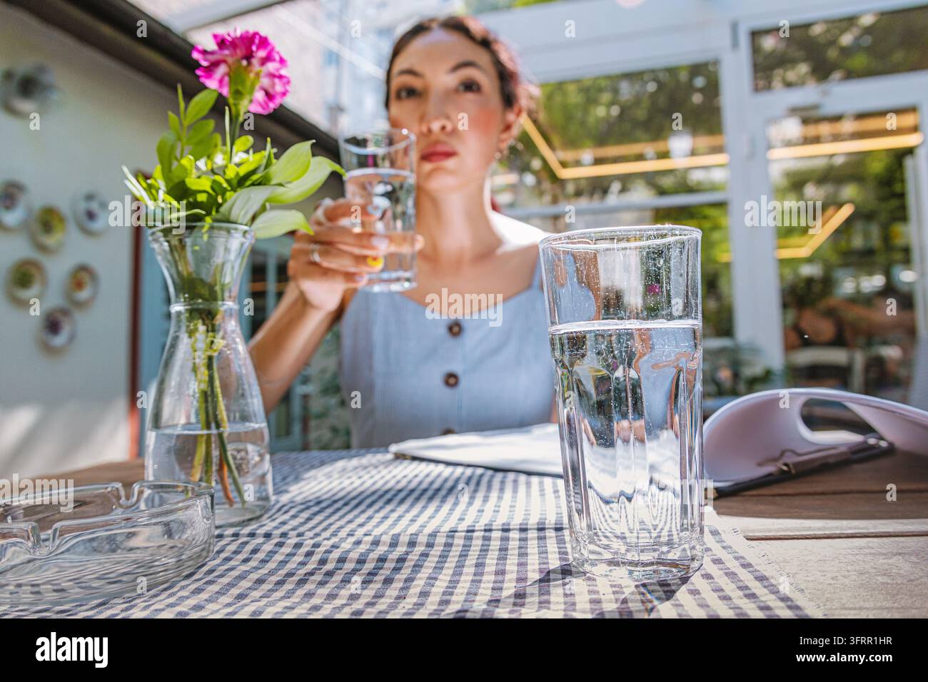 Momento di idratazione consapevole a un tavolo di caffè all'aperto soleggiato - ideale per marchi di benessere e stile di vita. Foto Stock