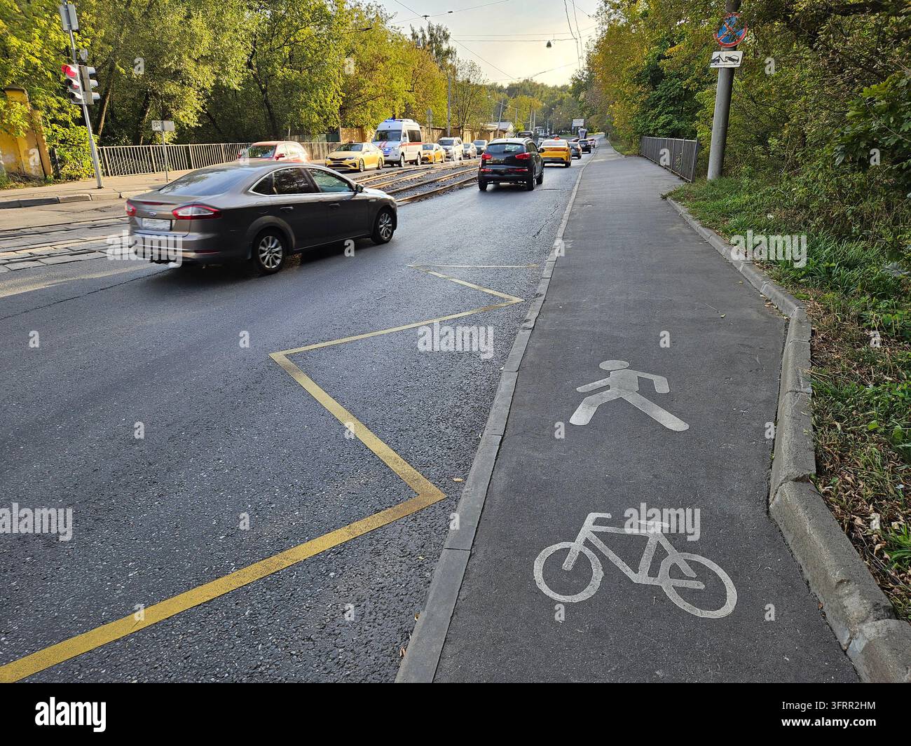 L'auto percorre una strada con una pista ciclabile sul lato. C'è un passaggio pedonale sul marciapiede Foto Stock