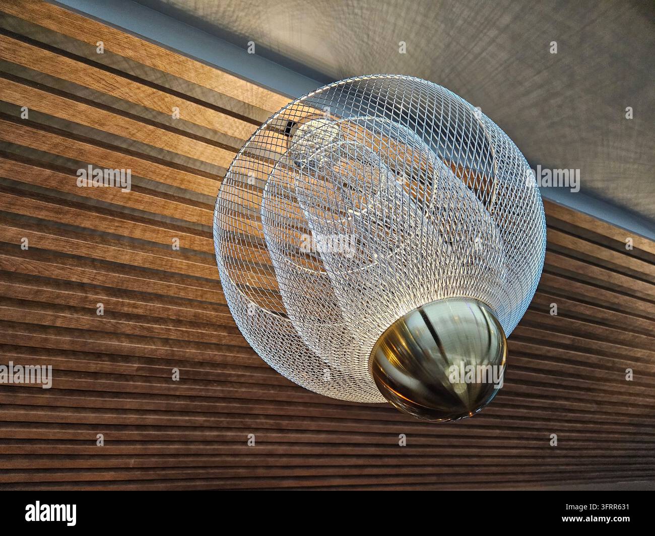 Apparecchio di illuminazione con base dorata e sfera argentata. L'apparecchio di illuminazione è sospeso dal soffitto Foto Stock