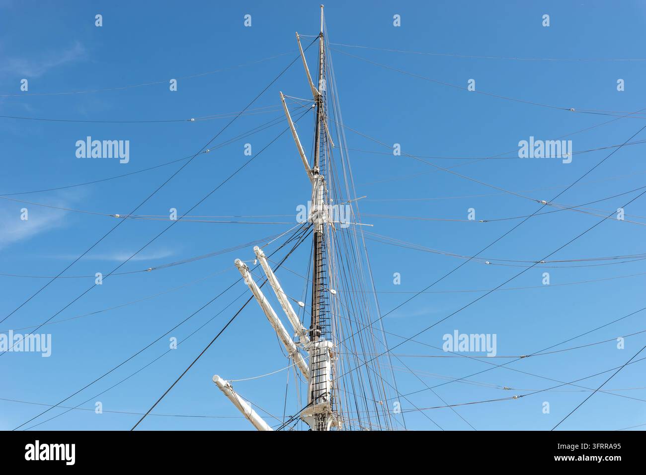Vista ad angolo basso degli alti alberi di una nave, delle aste e del sartiame che si stagliano contro un cielo blu limpido. Foto Stock