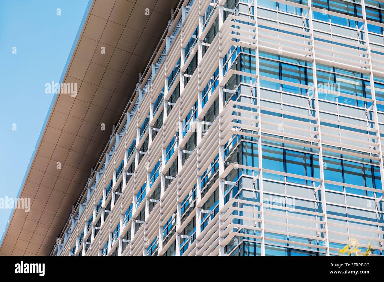 Facciata di un edificio di architettura moderna con pannelli di vetro, telai in acciaio e persiane orizzontali per parasole sotto un cielo blu limpido Foto Stock