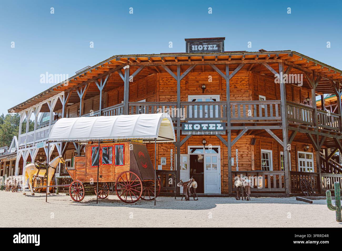 17 agosto 2026, parco a tema Zlatibor El Paso, Serbia: edificio alberghiero in legno in stile western con una carrozza coperta e una statua di cavallo, che evoca il frontier e Foto Stock