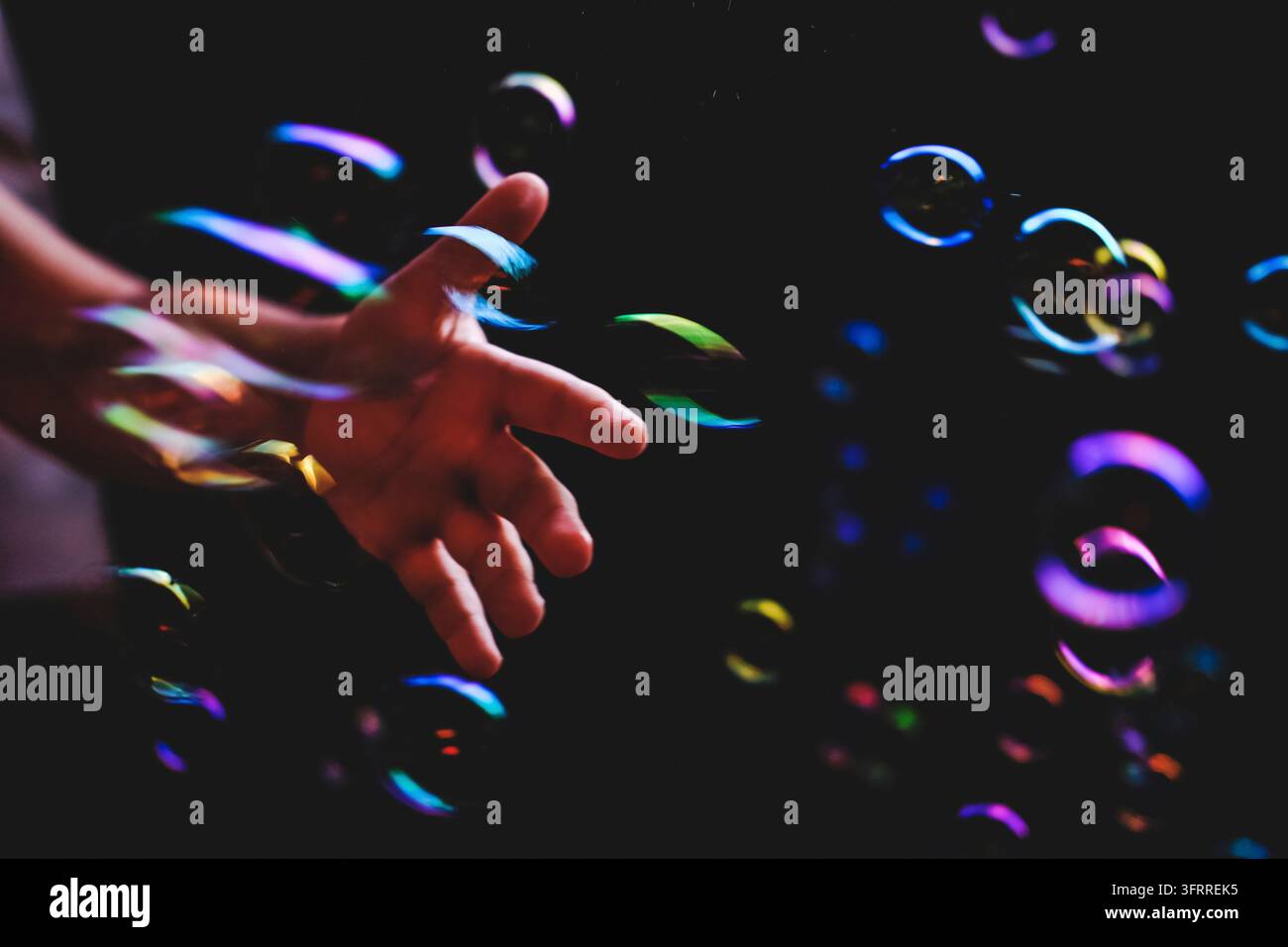 Bolle di sapone colorate volano su uno sfondo scuro e una mano umana cerca di catturarle Foto Stock