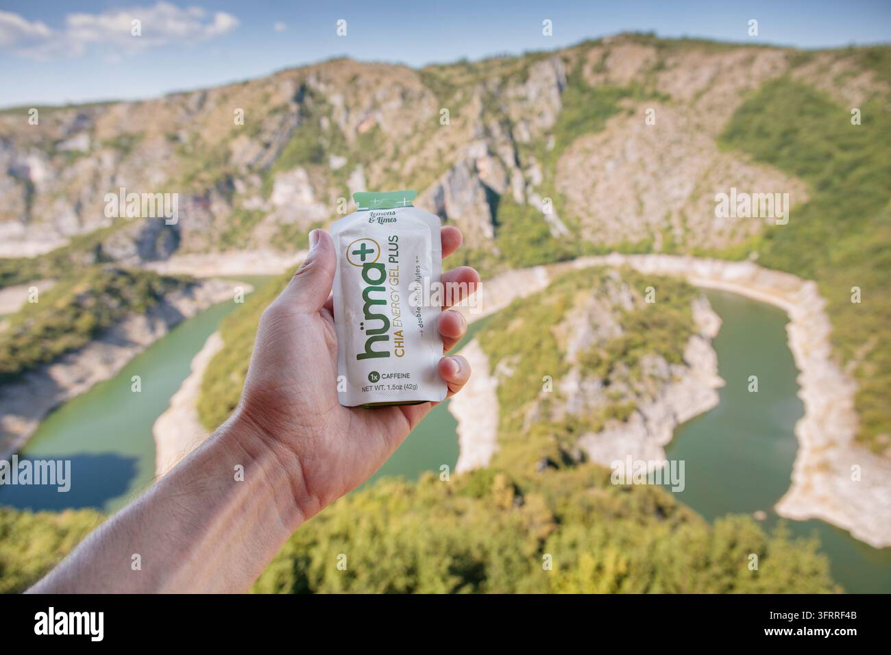 16 agosto 2026, Uvac, Serbia: Busta di integratore in gel energetico Huma tenuta davanti a uno sfondo drammatico di fiume nel canyon – ideale per il benessere e la salute all'aperto Foto Stock