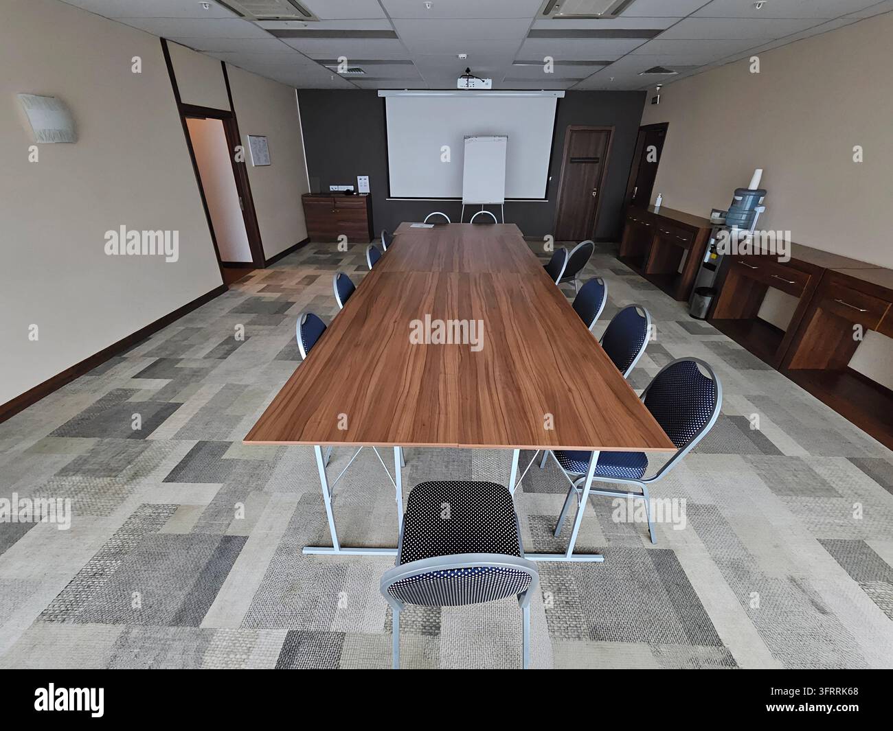 MINSK - 24 MARZO 2025: Un grande tavolo di legno con uno schermo per proiettore al centro. Ci sono molte sedie intorno al tavolo e alcune altre in fondo. La stanza è vuota Foto Stock
