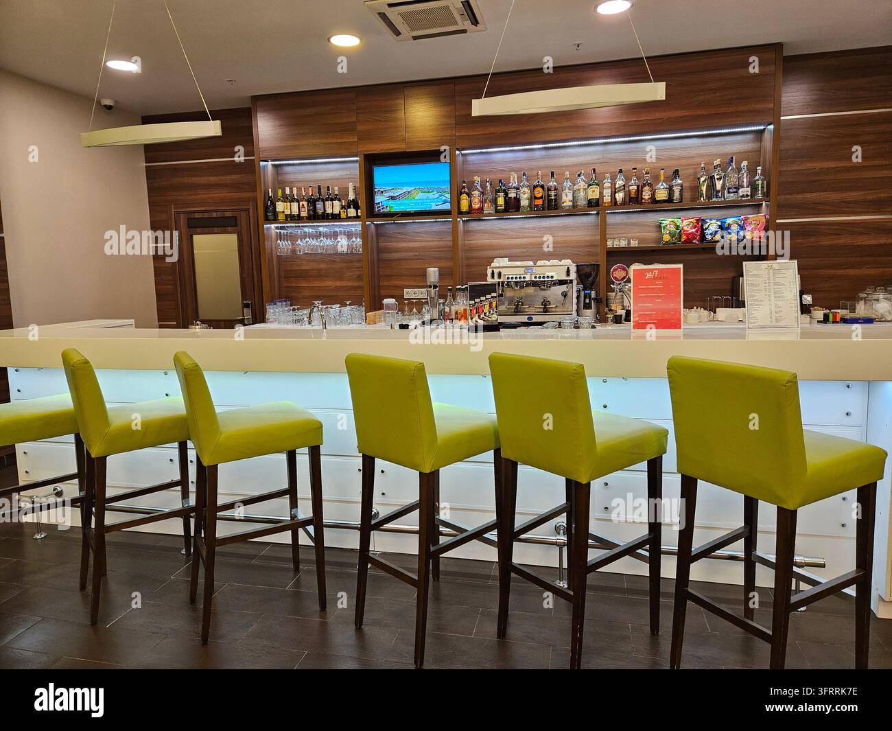MINSK - 24 MARZO 2025: Un bar con sedie verdi e una TV sul muro. Ci sono molte bottiglie sugli scaffali e un cartello sul muro Foto Stock