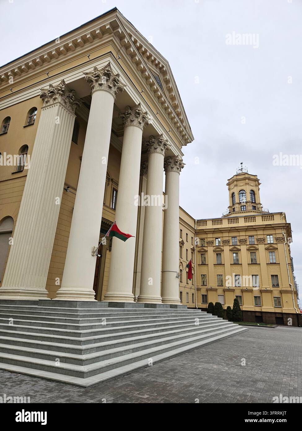MINSK - 25 MARZO 2025: Un alto edificio del servizio di sicurezza dello stato del KGB con una torre dell'orologio e una grande finestra. L'edificio è circondato da colonne. Il cielo è nuvoloso e il sole non è visibile Foto Stock