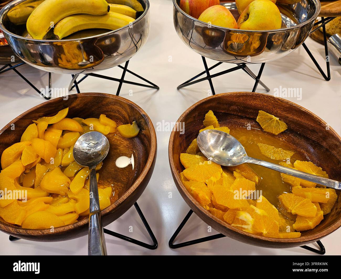 Una ciotola di arance a fette è accanto a una ciotola di pesche a fette. C'è un cucchiaio in ogni ciotola. banane e mele Foto Stock