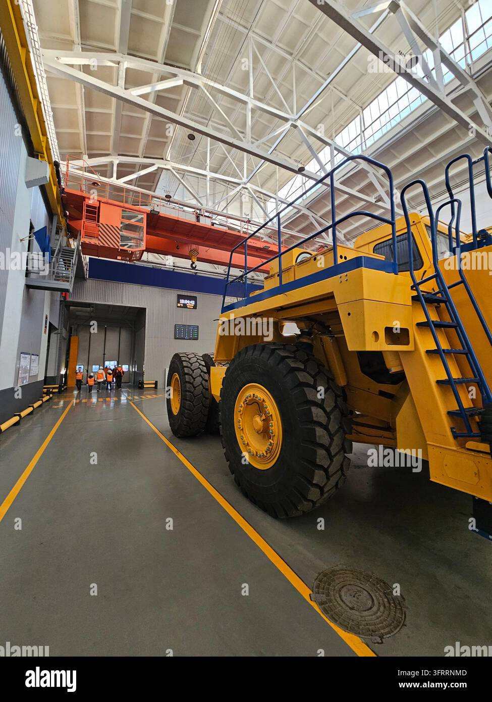 Un grande camioncino giallo e blu è parcheggiato in un grande edificio. L'edificio ha un tetto bianco ed è circondato da una linea gialla Foto Stock